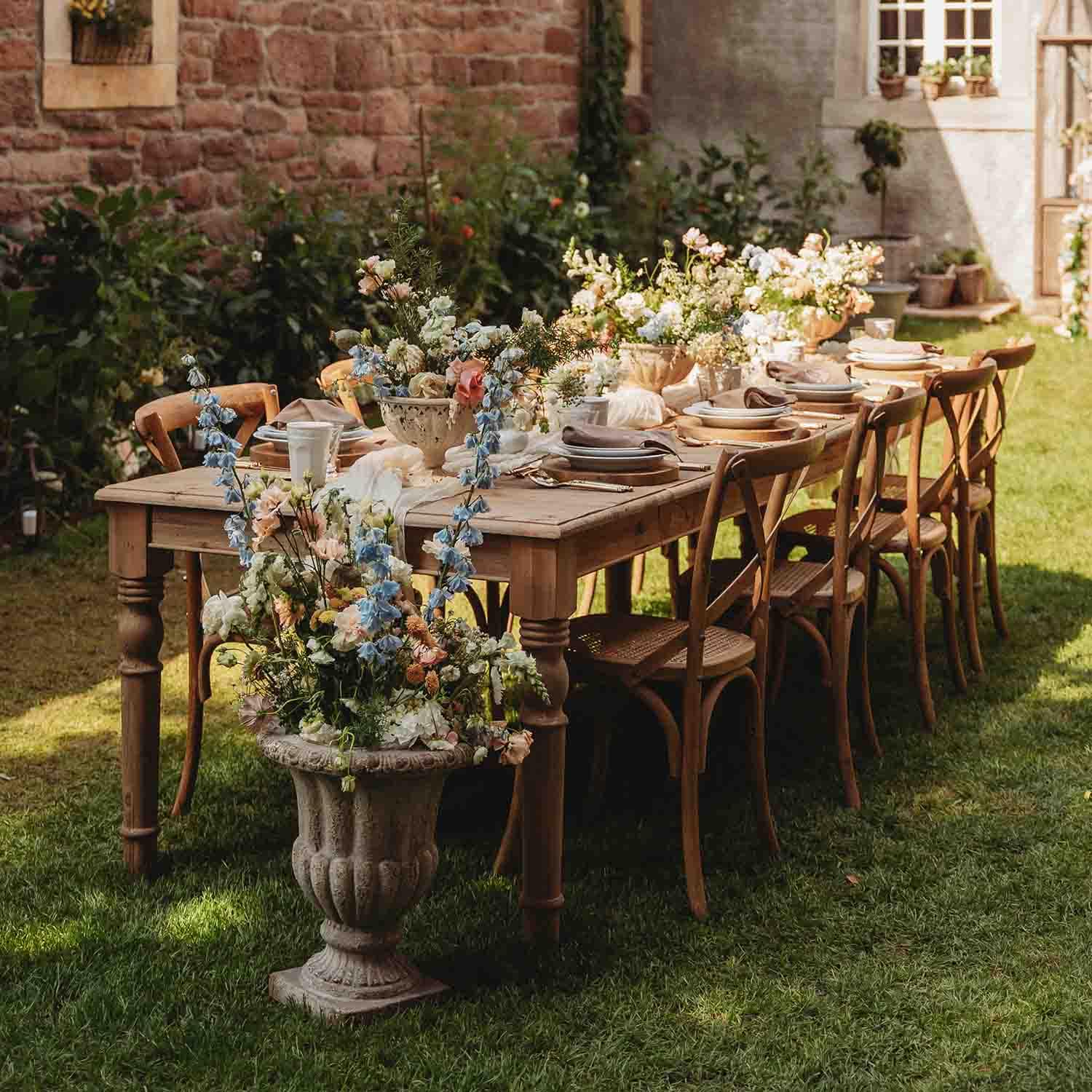Holztisch im Garten mit Blumenarrangements und gedecktem Geschirr bei Sonnenschein