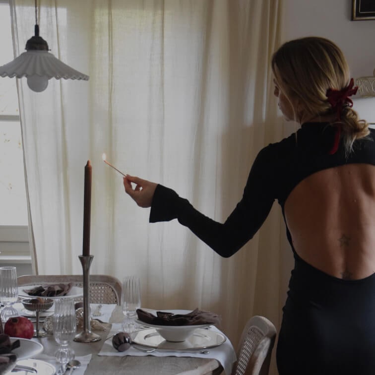Frau im schwarzen Rückenfreien Kleid zündet Kerze an einem elegant gedeckten Esstisch an