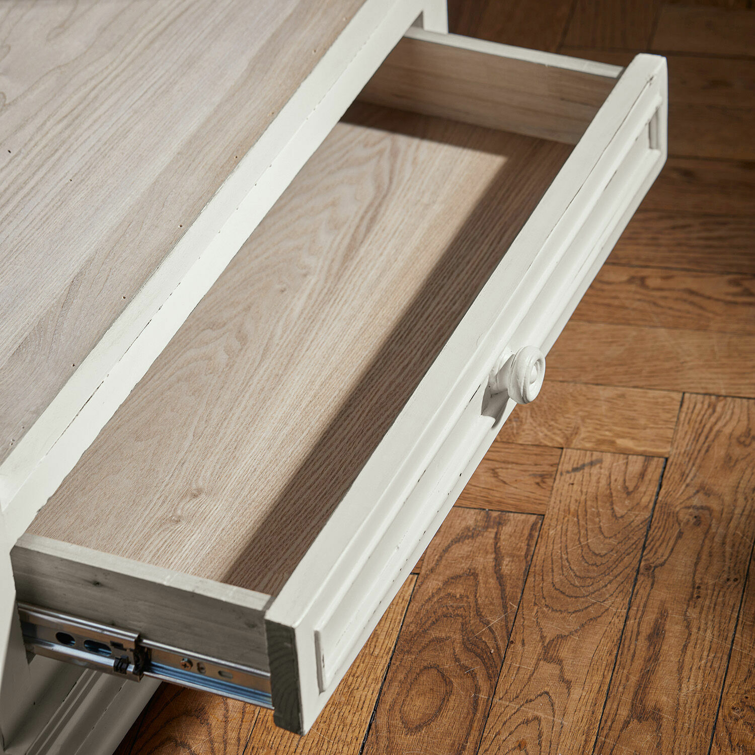 Offene weiße Holzschublade mit rundem Griff auf hellem Holzboden im Vintage-Stil