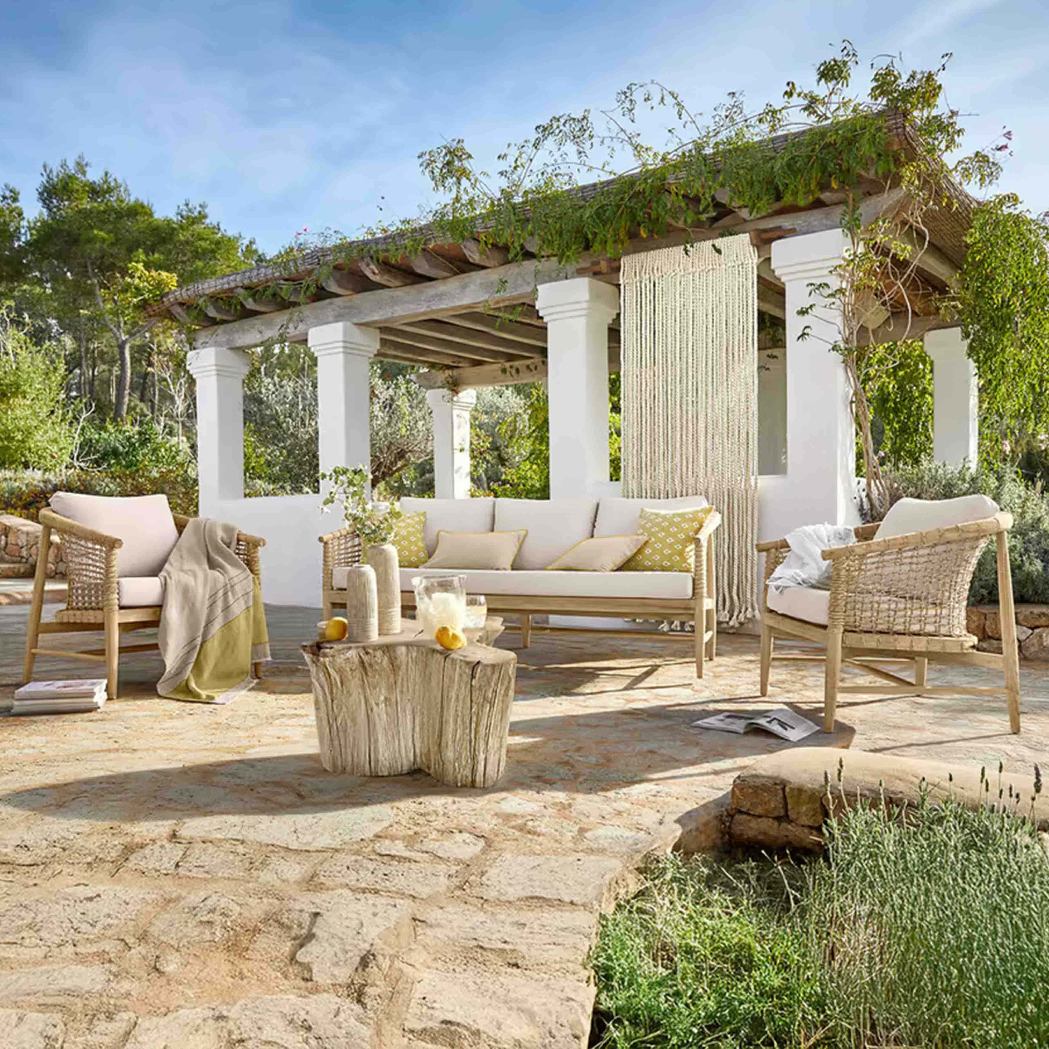 Gartenmöbel-Set aus hellem Holz mit beigen Polstern auf Steinpatio unter einer begrünten Pergola