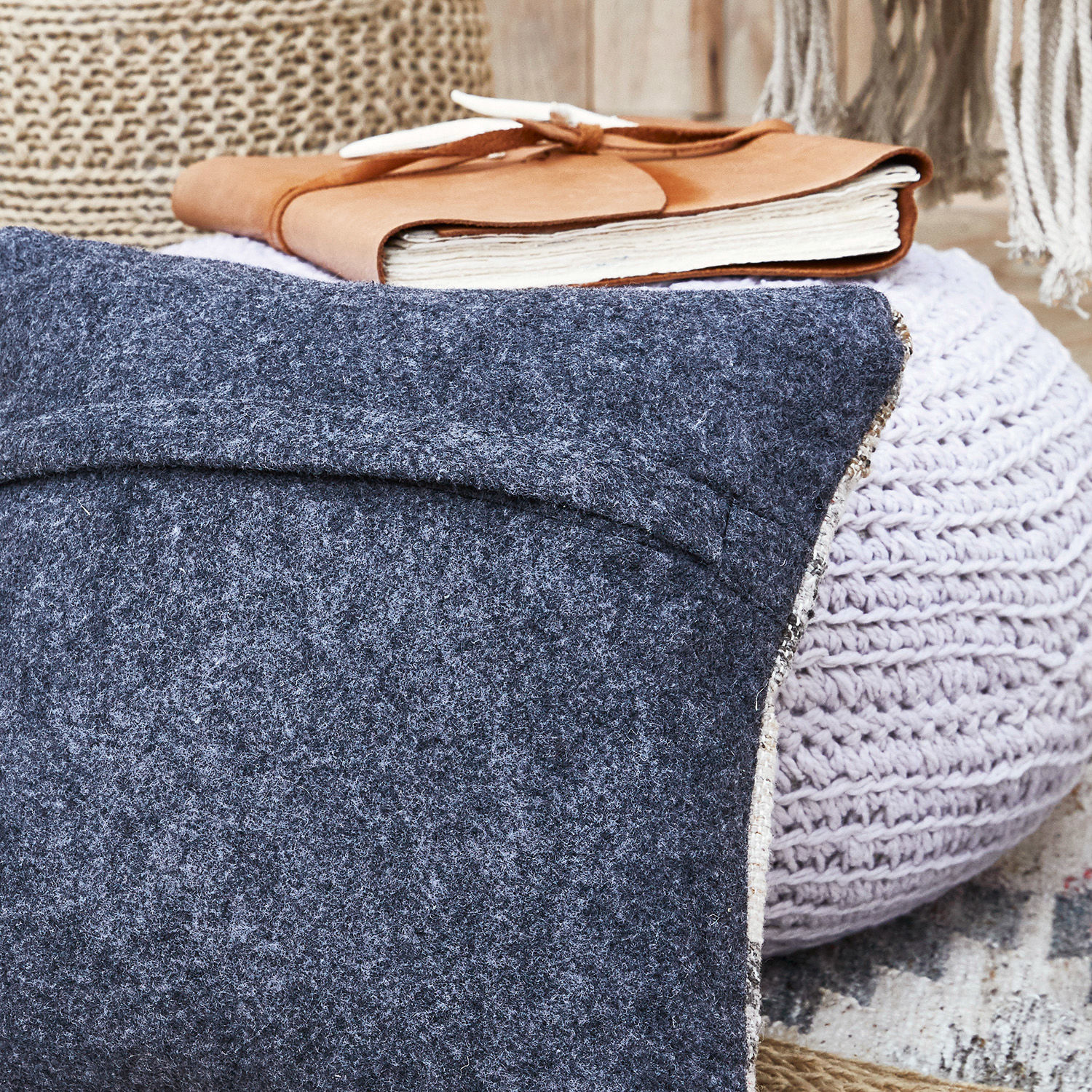 Graue Wolldecke auf hellrosa gestricktem Pouf mit braunem Leder-Notizbuch im Hintergrund
