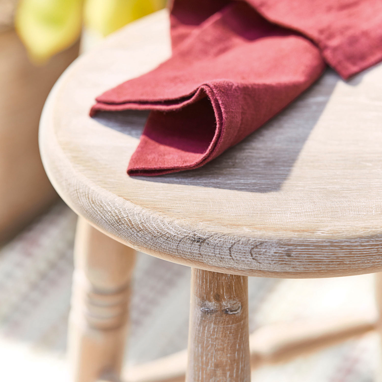 Tischplatte aus hellem Holz mit rotem Leinentuch bei natürlichem Licht und Stoff im Hintergrund