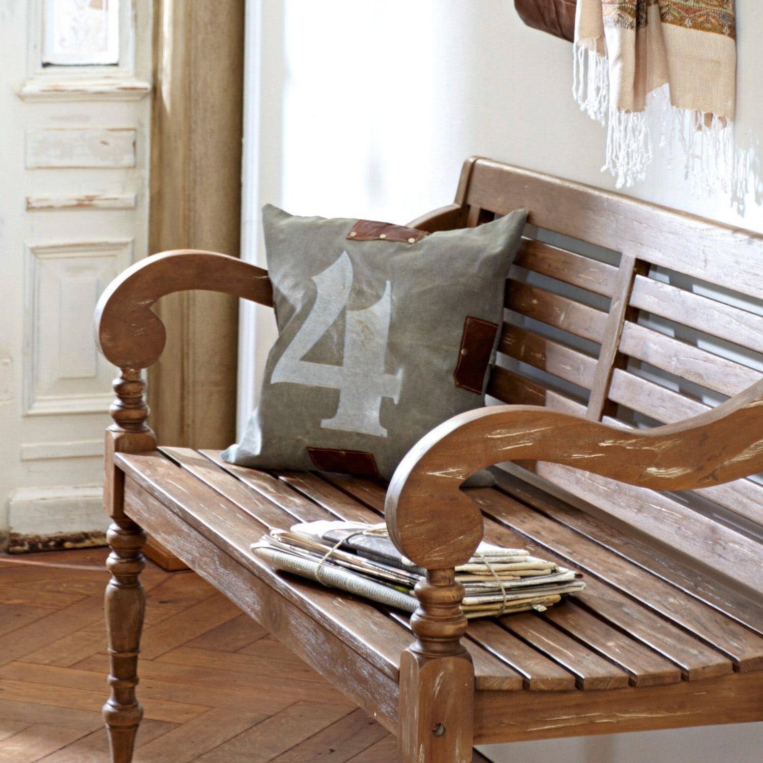 Kissen N° 4 Holzbank mit grauem Dekokissen mit Zahl 4 und einem Stapel Zeitungen in hellem Raum