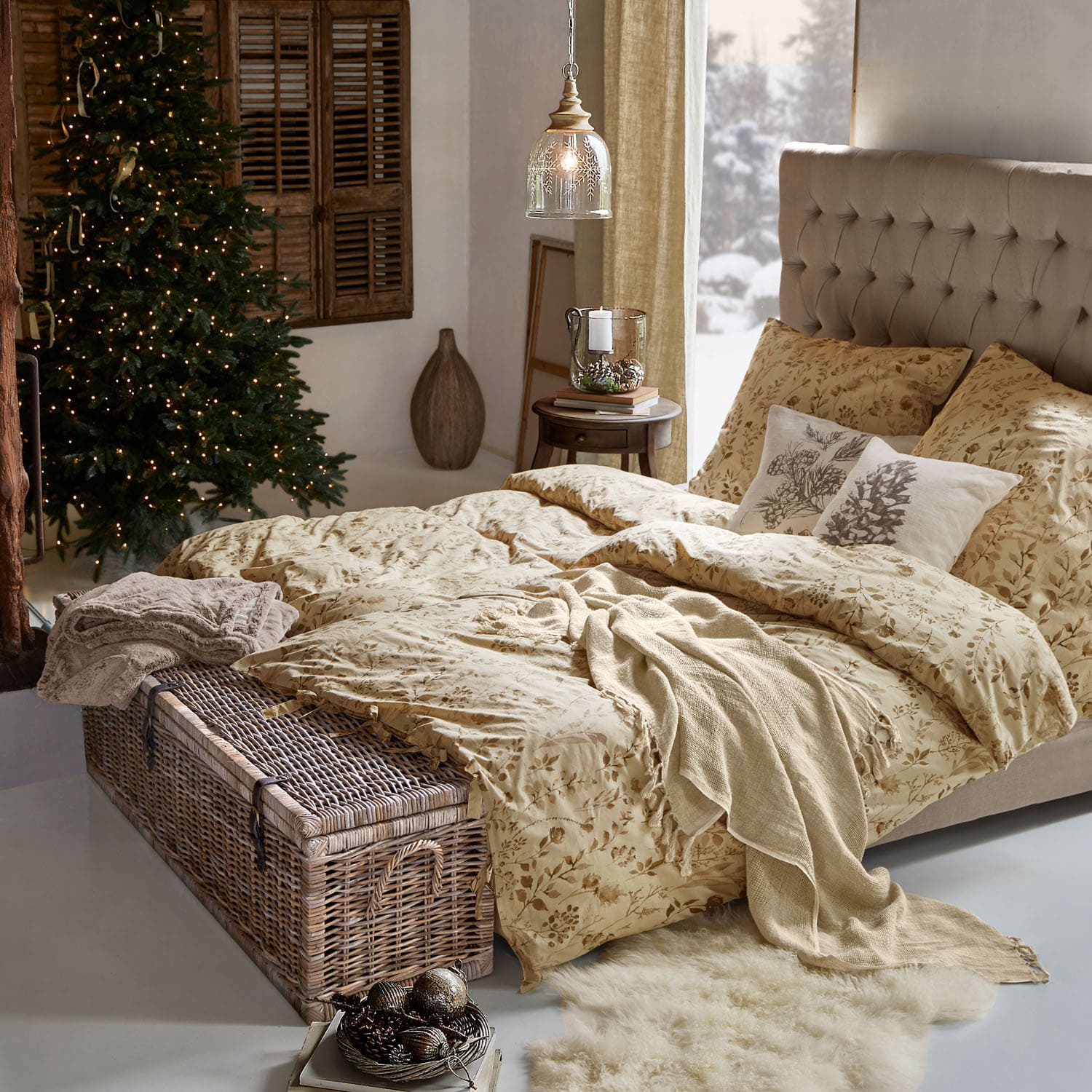 Gemütliches Schlafzimmer mit beiger Bettwäsche mit Blumenmuster und Korbtruhe am Fußende