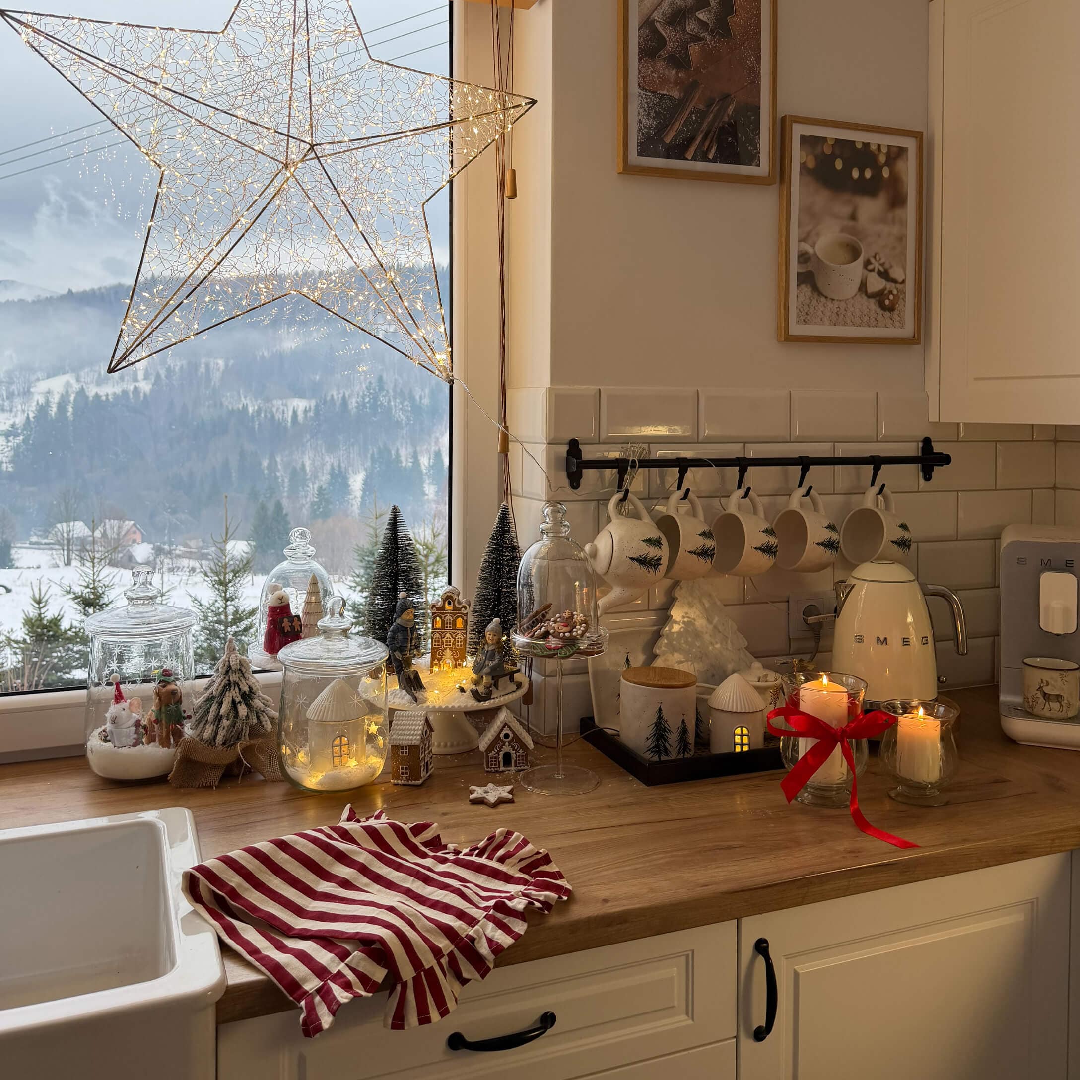 Küche mit Holzarbeitsplatte und Weihnachtsdekoration, weiße Tassen mit Tannenbaum-Motiv und LED-Lichterkette