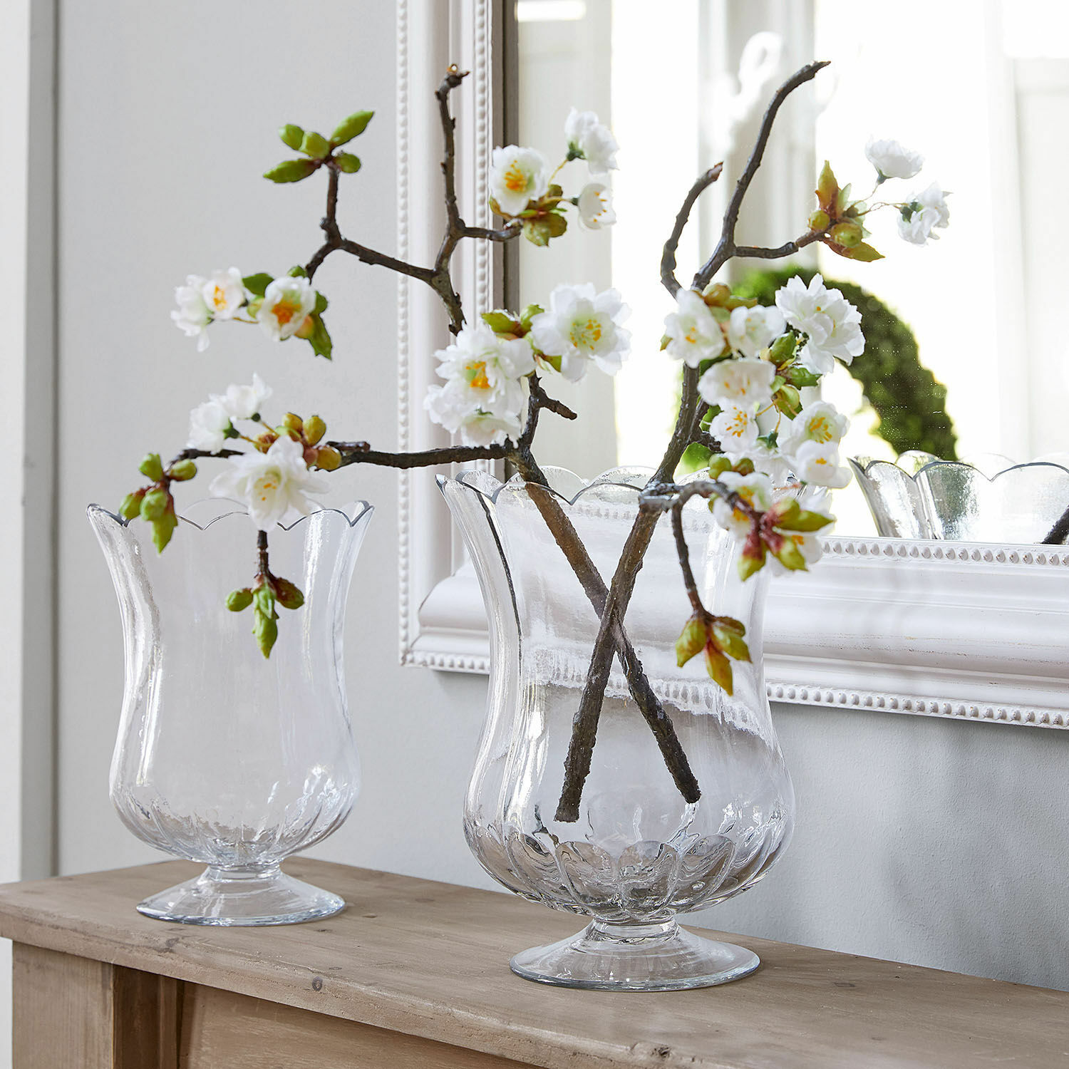 Dekoblume 2er Set Gráda Transparente Glasvasen mit welligem Rand auf Holztisch mit weißen Dekoblumen arrangiert