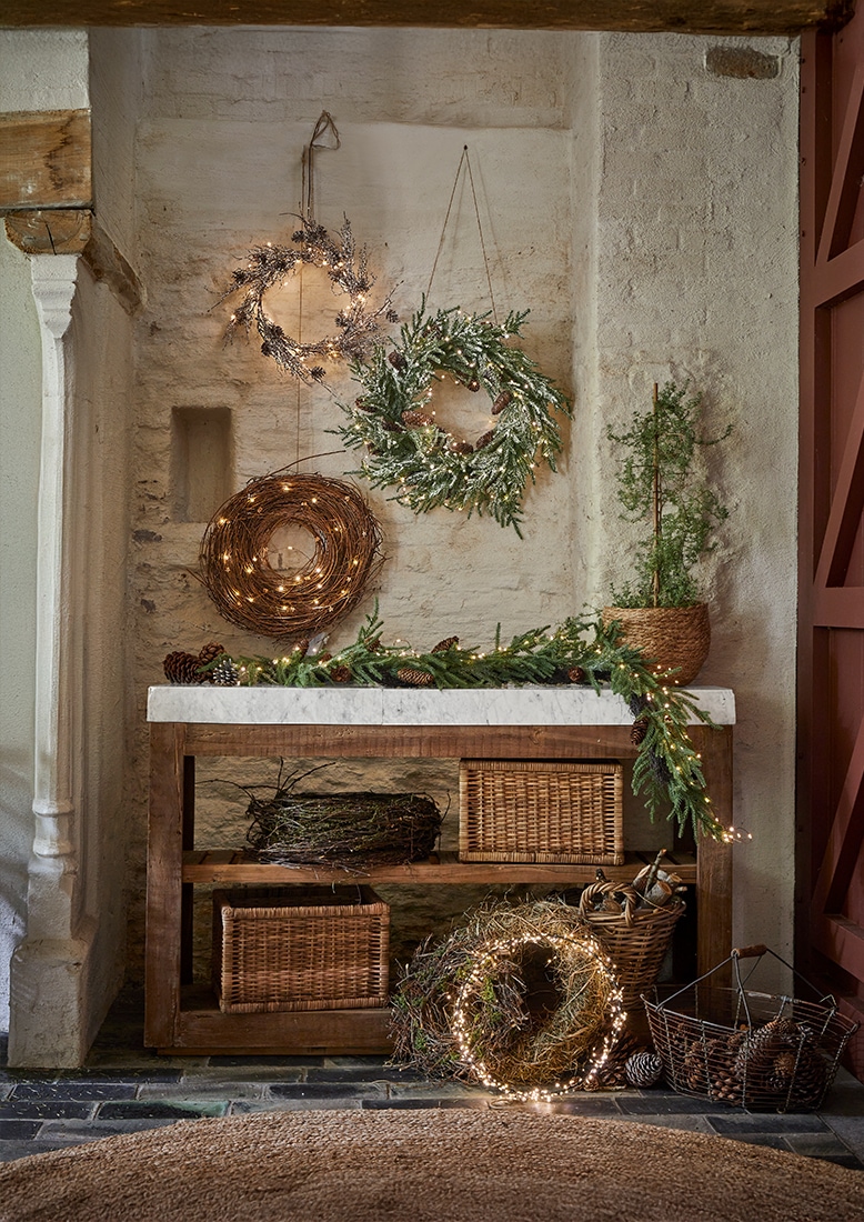 Weihnachtliche Dekokränze aus Zweigen und Lichterketten an Wand und Holztisch mit Marmorplatte