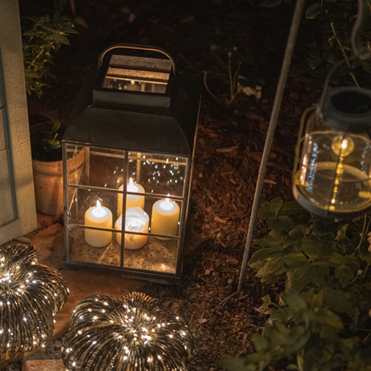 Metalllaterne mit vier weißen Kerzen und dekorativen Lampions im Garten bei Nacht