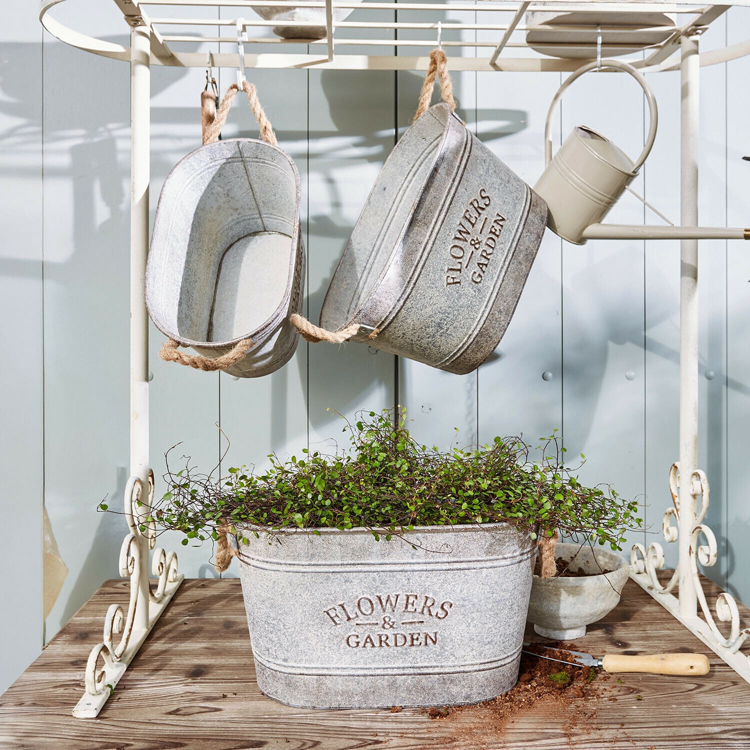Übertopf 3er Set Merrin Graue Metallpflanzgefäße mit Aufschrift Flowers & Garden, grüne Pflanze und Gartengerät auf Holztisch