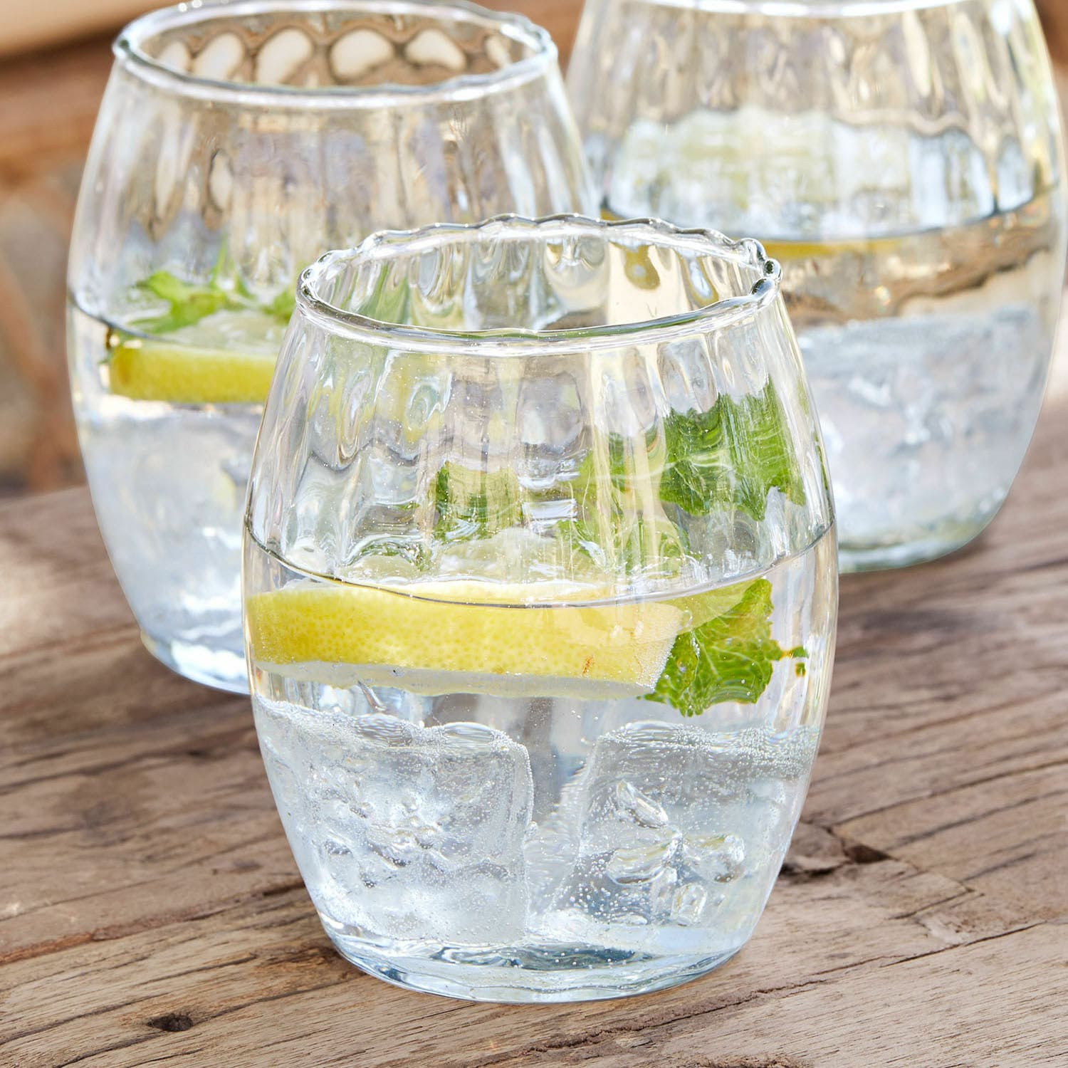 Gläser aus klarem Glas mit Eis, Zitronenscheibe und Minze auf Holztisch