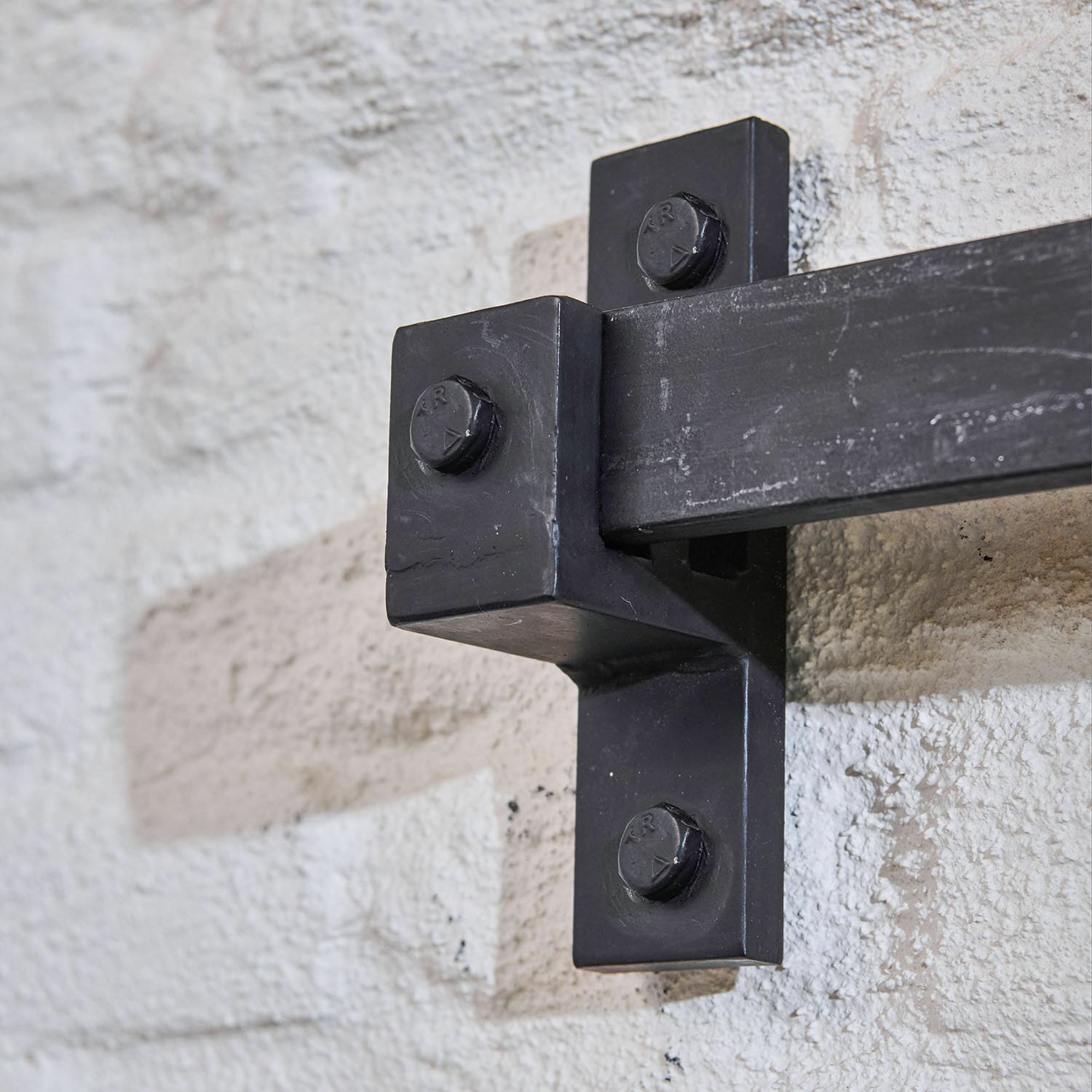 Schwarze Metall-Wandhalterung mit vier Schrauben an heller strukturierter Wand, dekoratives Element
