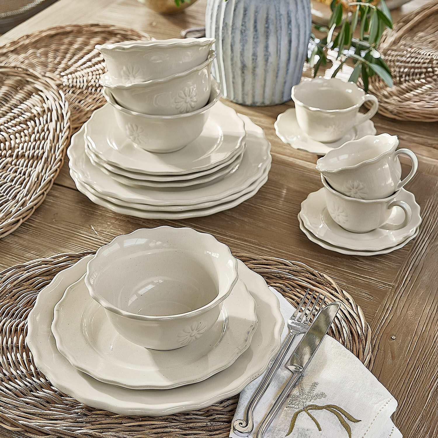 Set aus cremefarbener Keramik mit Tellern und Tassen auf geflochtenen Platzsets im Landhausstil