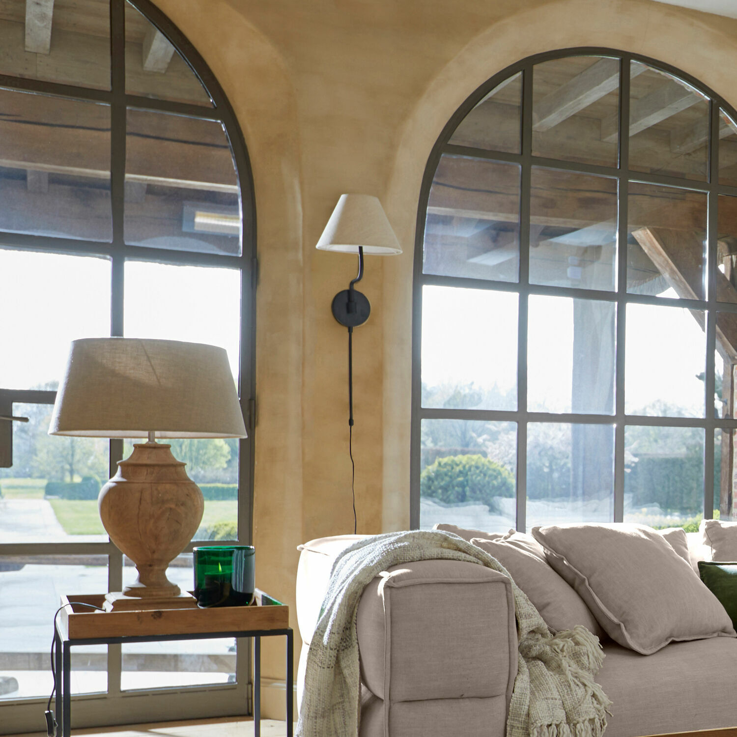 Gemütliches Wohnzimmer mit beigem Sofa, Holztischlampe und großen Fenstern mit Metallrahmen