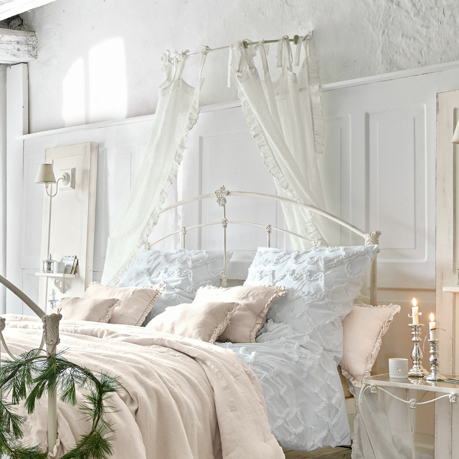 Gemütliches Schlafzimmer mit weißem Metallbett, beiger Leinenbettwäsche, dekorativen Vorhängen und Kerzenhaltern