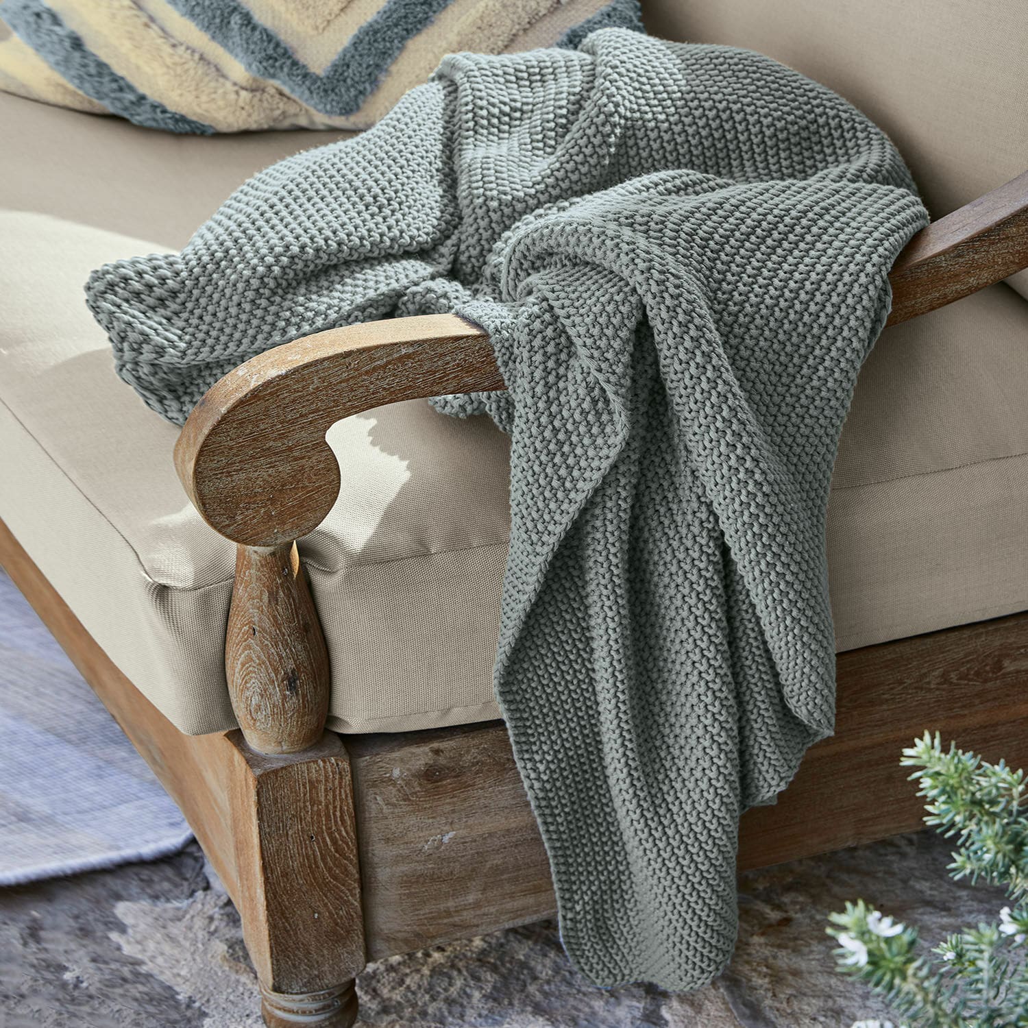 Plaid Ancy Grau gestrickte, dicke Decke aus weicher Wolle auf einem Holzstuhl mit beigem Polster