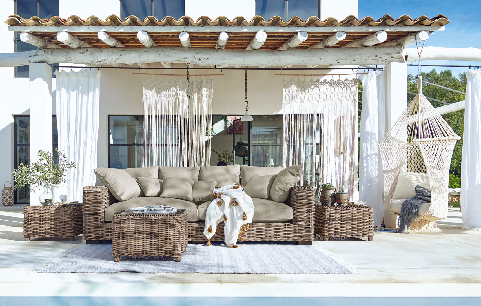 Gartenmöbel-Set aus Rattan mit beigen Polstern auf Terrasse mit Hängesessel und Boho-Dekor