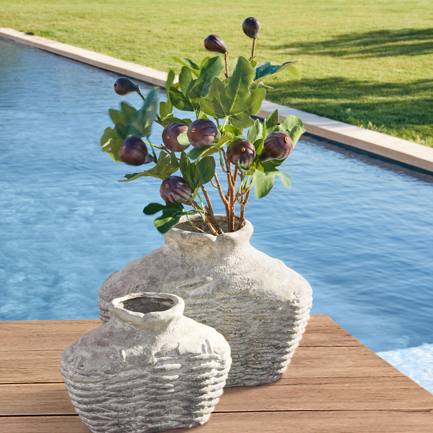 Zwei rustikale graue Keramikvasen auf Holztisch am Pool mit grünen Blättern und Früchten