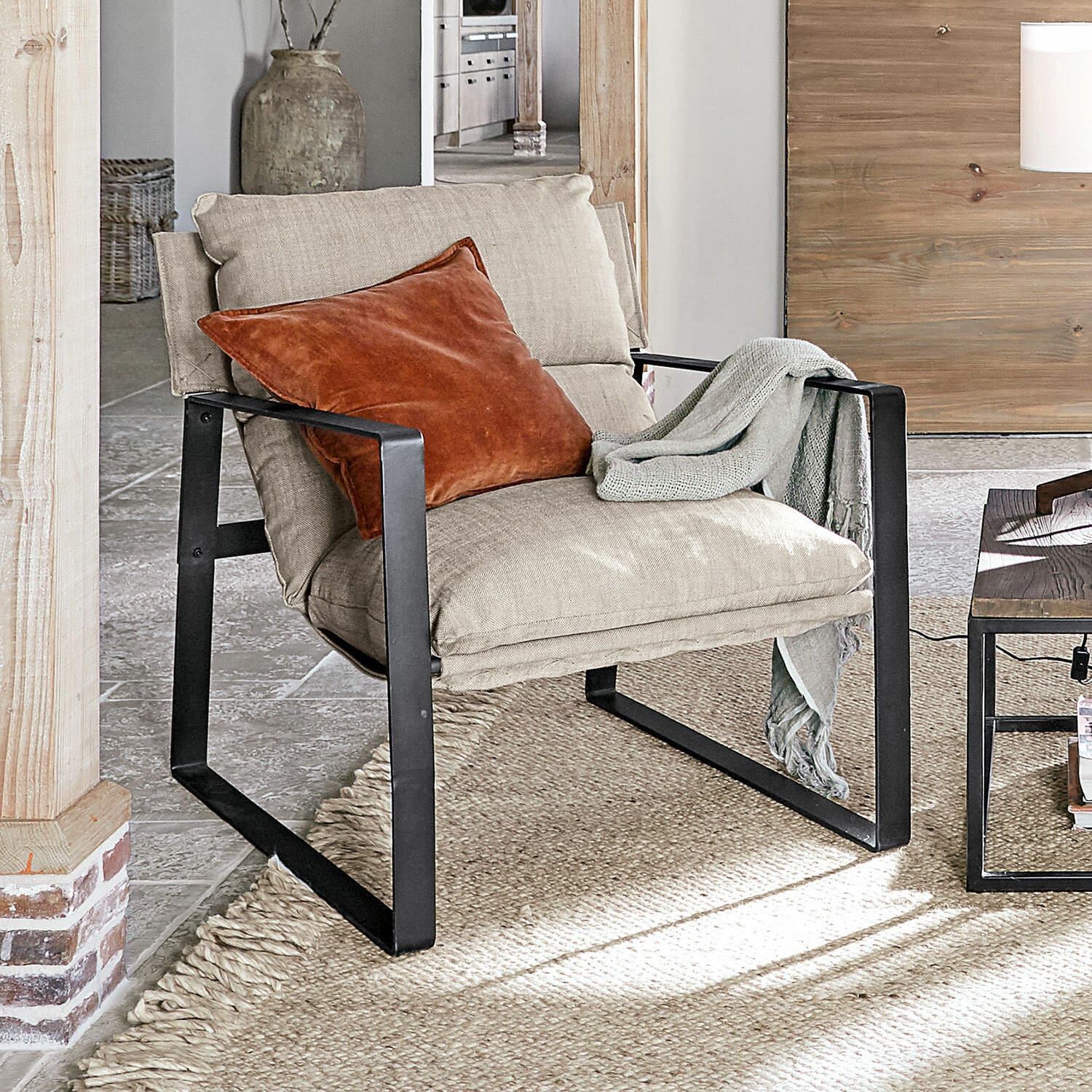Sessel Seuvard Beiger Polsterstuhl mit schwarzem Metallgestell, orangefarbener Kissen und grauem Plaid im Wohnzimmer