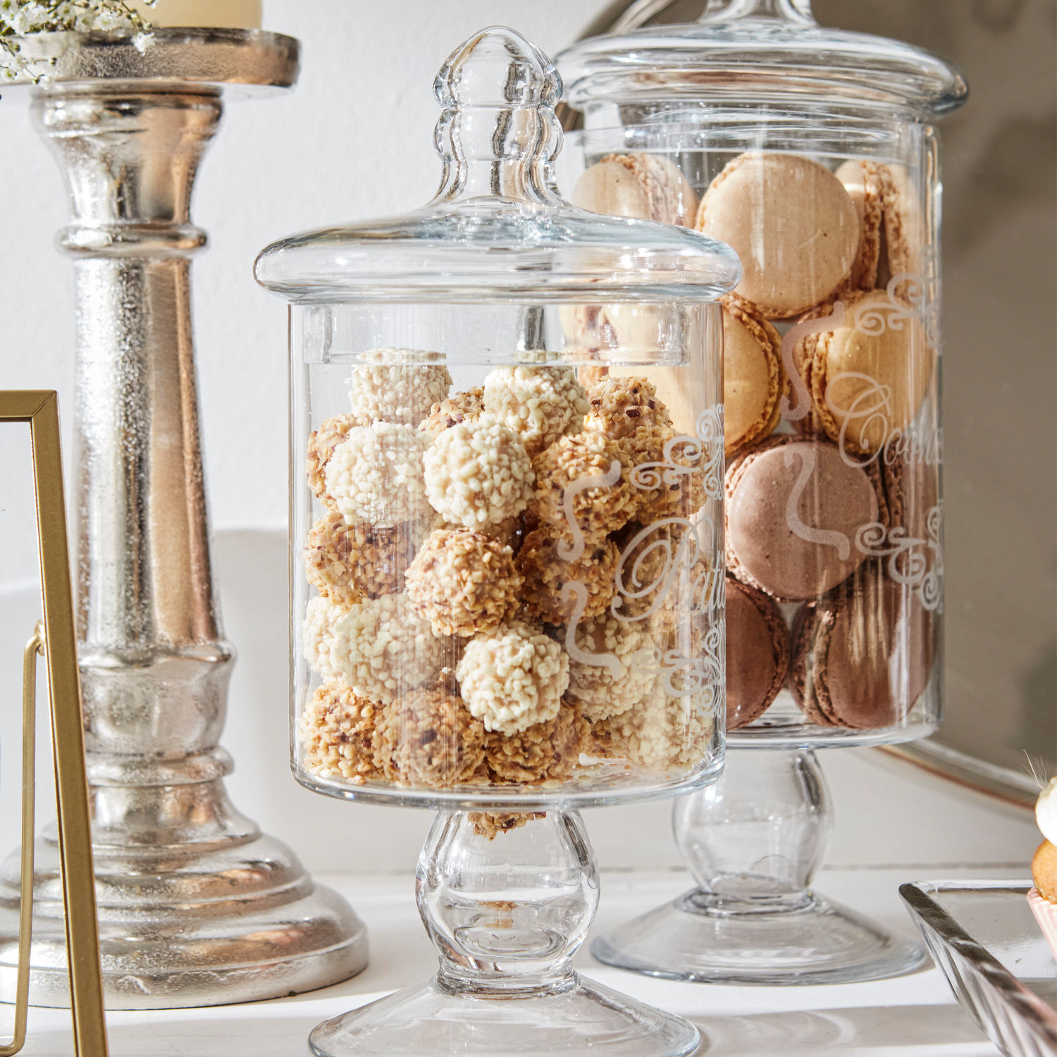 Glasgefäß mit Deckel und Fuß gefüllt mit Schokoladenkugeln und Macarons