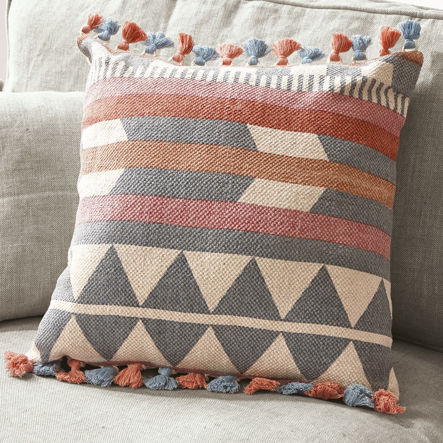 Dekoratives Baumwollkissen mit geometrischem Muster und blauen sowie orangen Quasten auf hellem Sofa