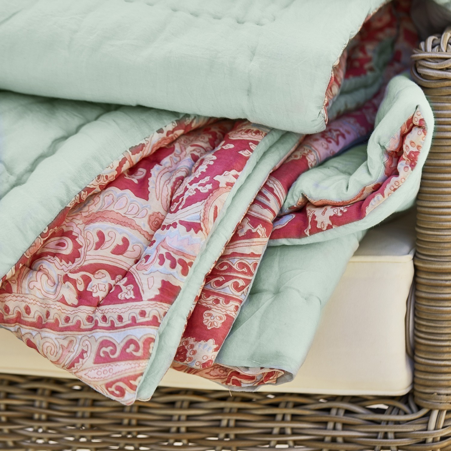 Weiche grüne Baumwolldecke mit rotem Paisley-Muster auf einem Korbsessel