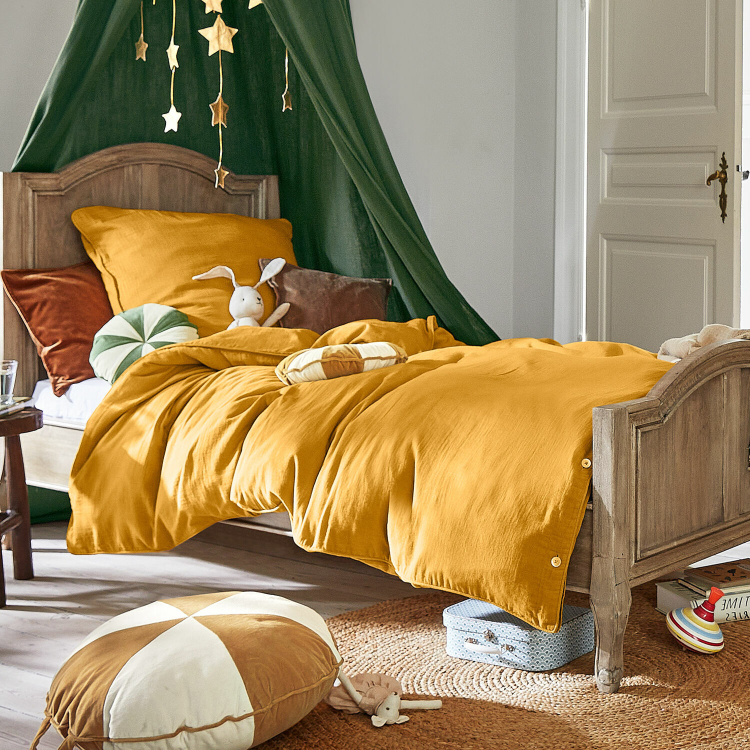 Kinderbett aus Holz mit senfgelber Leinenbettwäsche, goldene Stern-Deko und Plüschhase