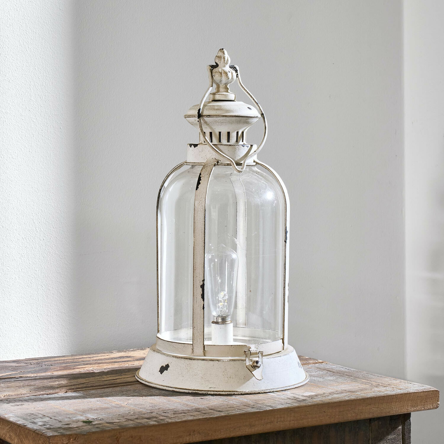 Weiße Metalllaterne mit klarem Glas und dekorativem Griff auf einem Holztisch