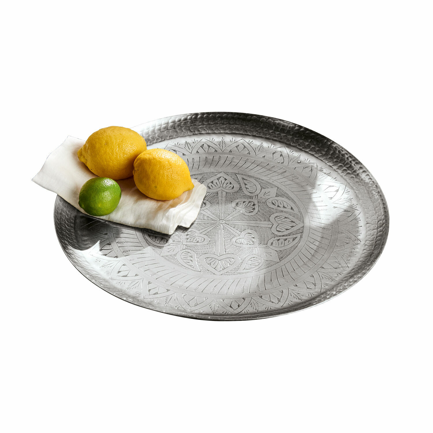 Rundes Metalltablett mit graviertem Muster in Silber, darauf Zitronen und Limette auf weißer Serviette