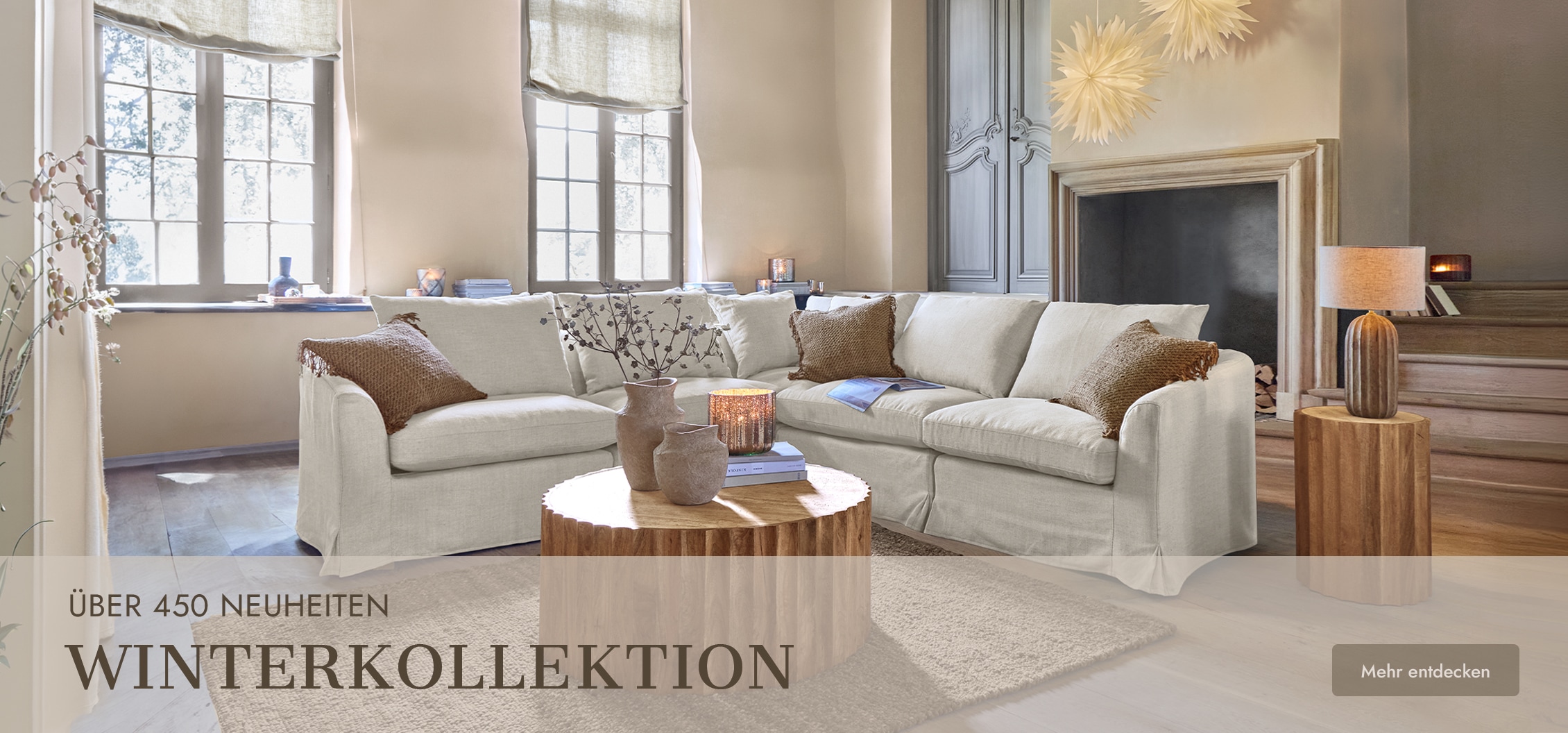 Gemütliches Wohnzimmer mit beigem Ecksofa aus Stoff und rundem Holztisch in Winterkollektion-Atmosphäre