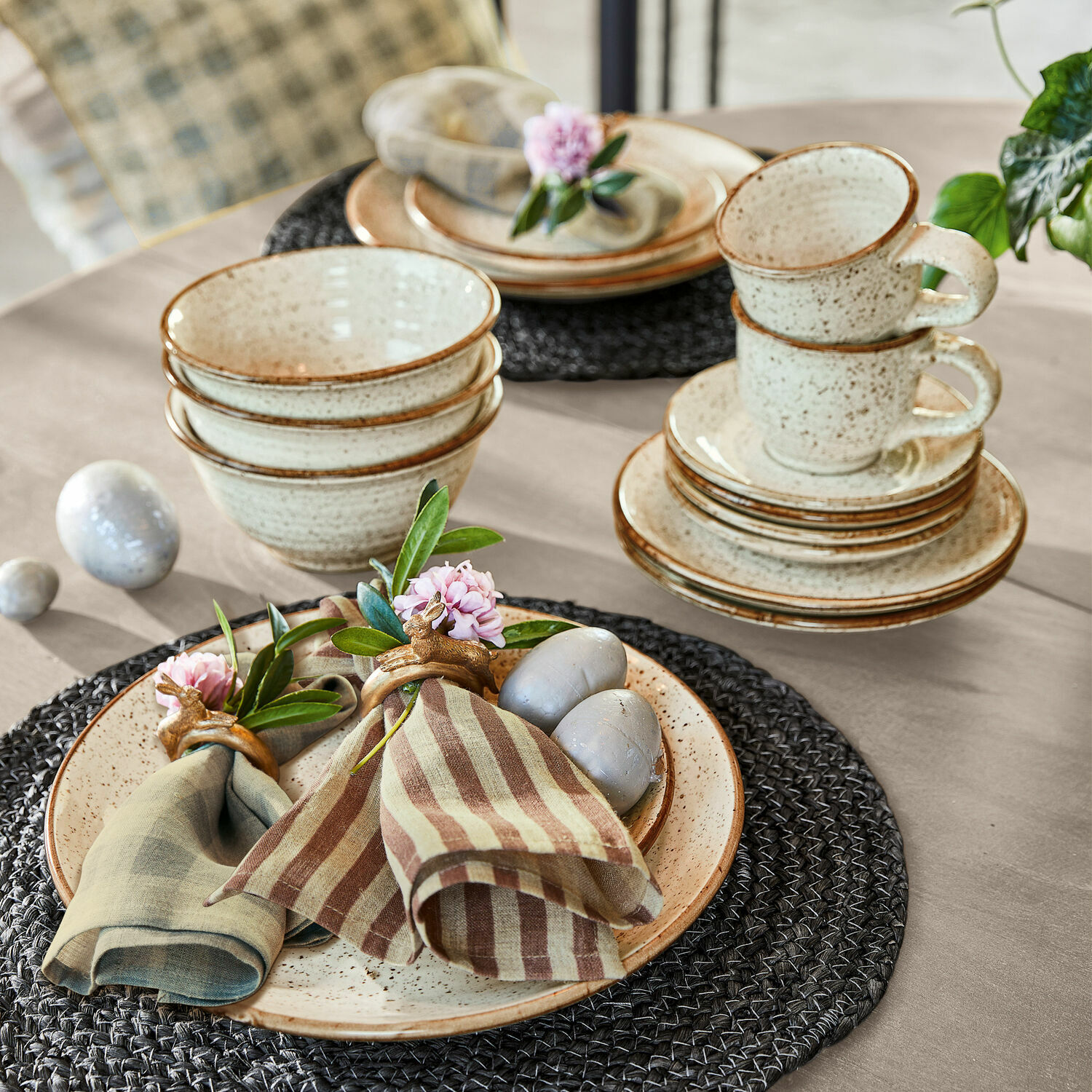 Keramik-Geschirrset in Creme mit braunen Rändern auf grauem Platzset aus geflochtenem Material