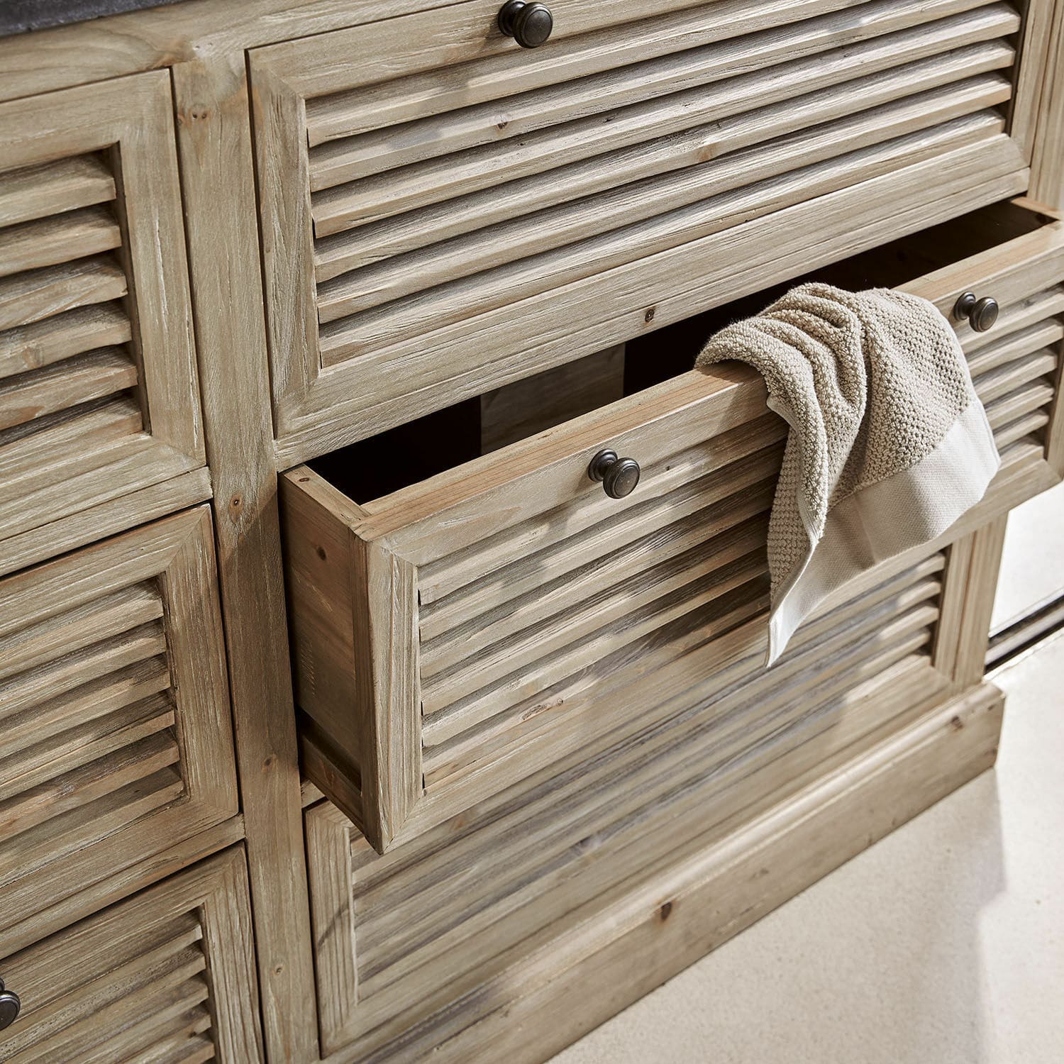 Holzschrank in Naturfarbe mit Lamellentüren und geöffneter Schublade mit beigem Handtuch