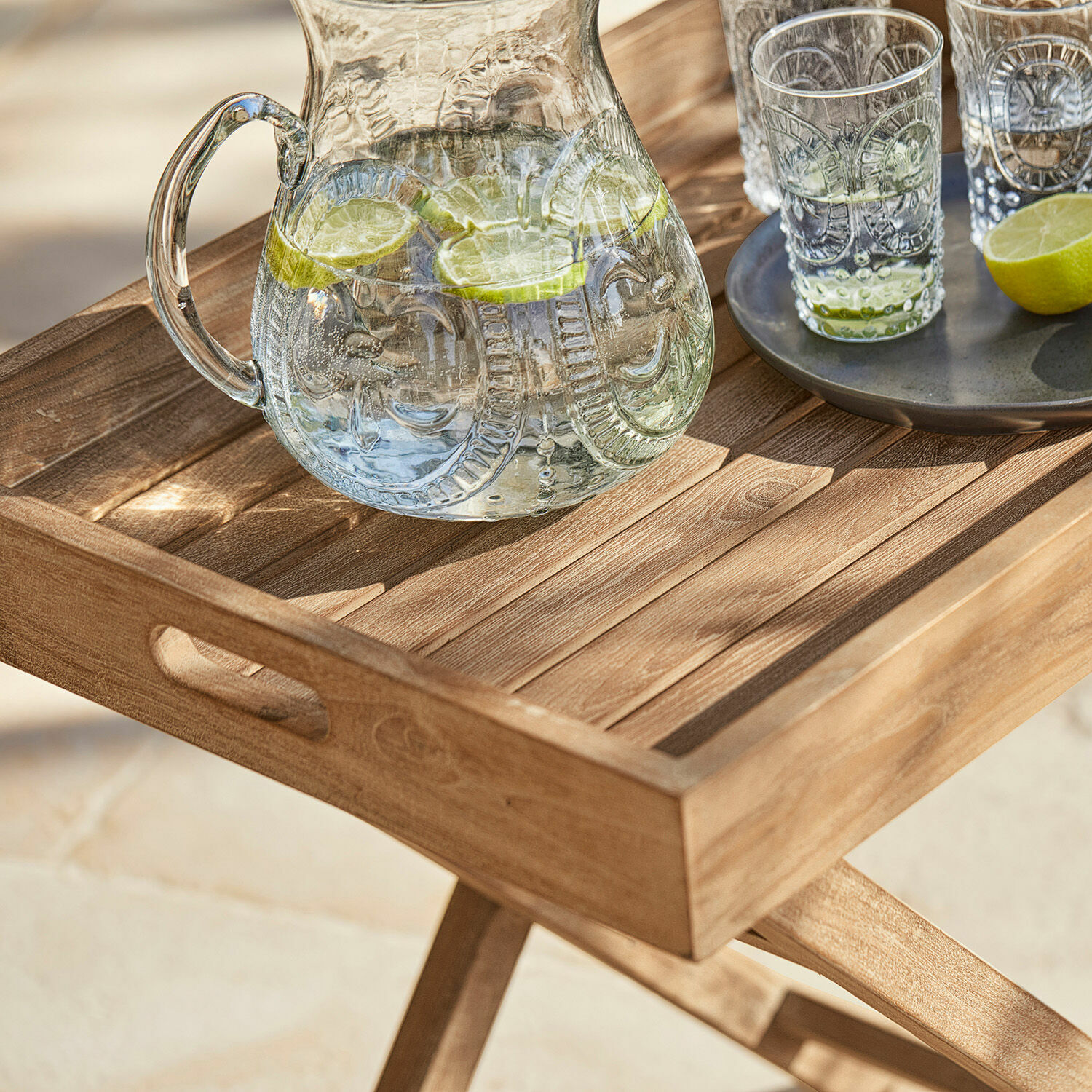 Holztablett auf klappbarem Gestell mit Krug und Gläsern mit Limettenwasser auf Terrasse