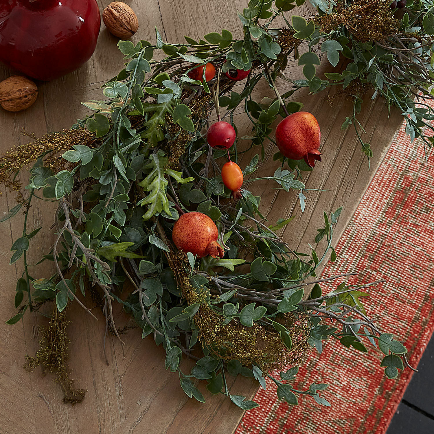 Dekorativer Kranz aus grünen Blättern und roten Früchten auf Holztisch mit Teppich