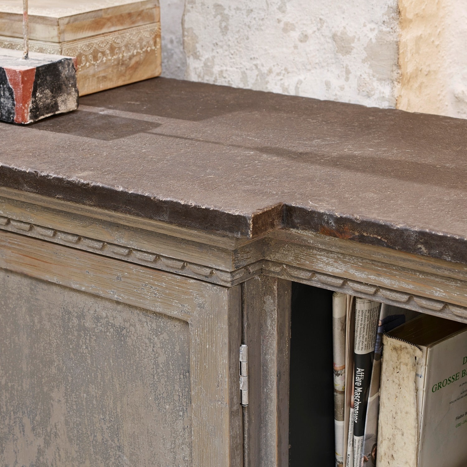 Dunkle Steinplatte auf antik wirkendem Holzschrank mit Büchern im Inneren