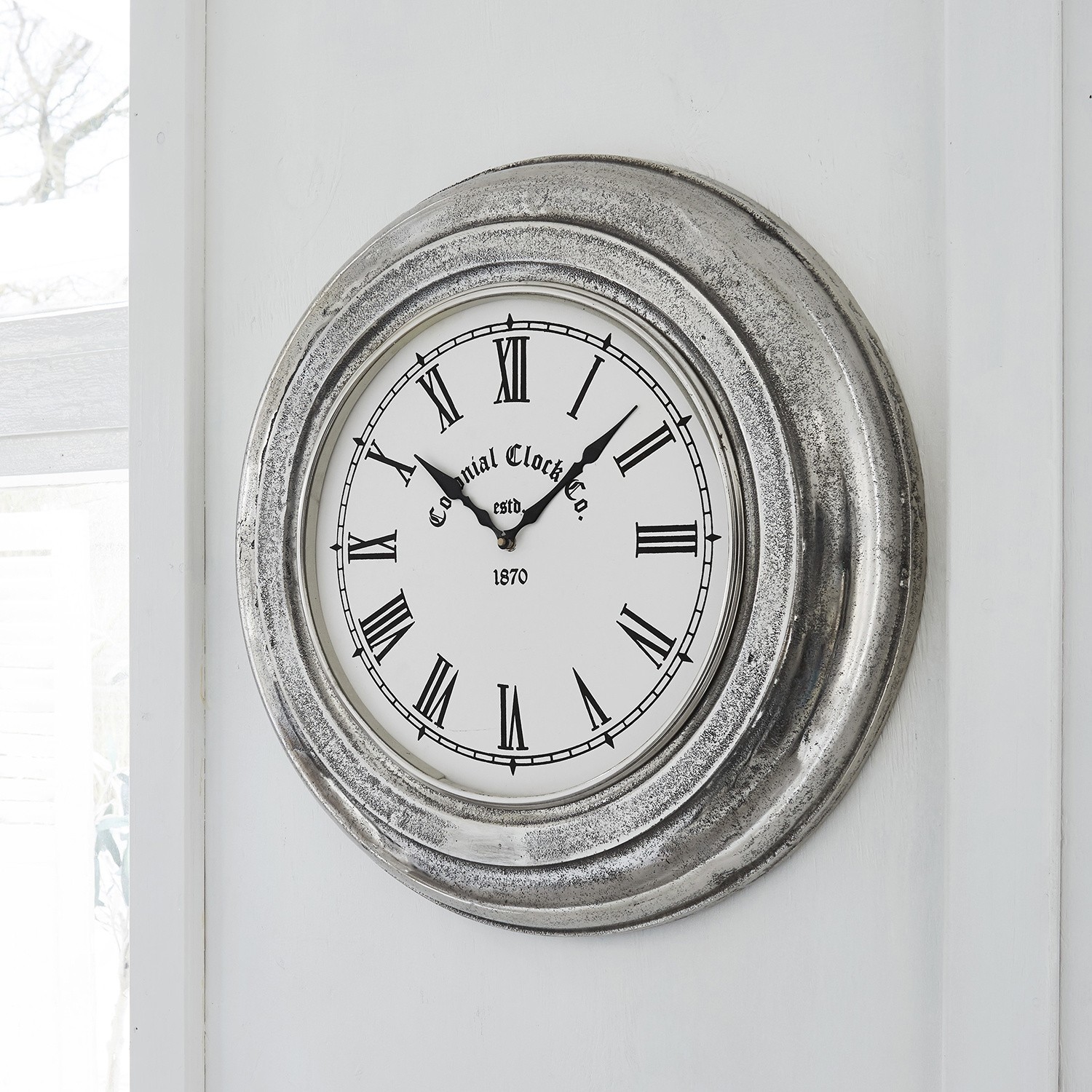 Runde Wanduhr mit silbernem Metallrahmen, römischen Ziffern und weißem Zifferblatt