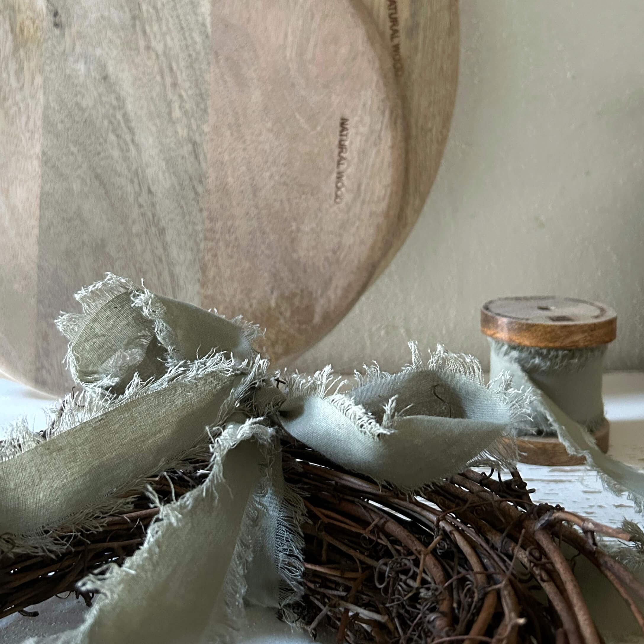 Natürlicher Holzteller mit grauem Leinenband auf Weidenkranz als Wohnaccessoire