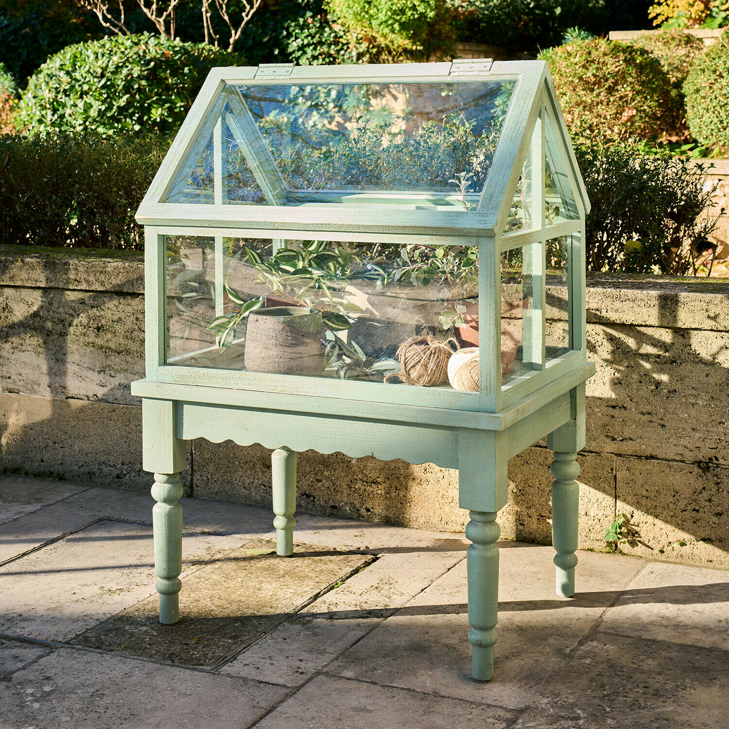 Kleine grüne Holz-Gewächshaus auf Beinen mit Pflanzen und Garnrollen für den Garten