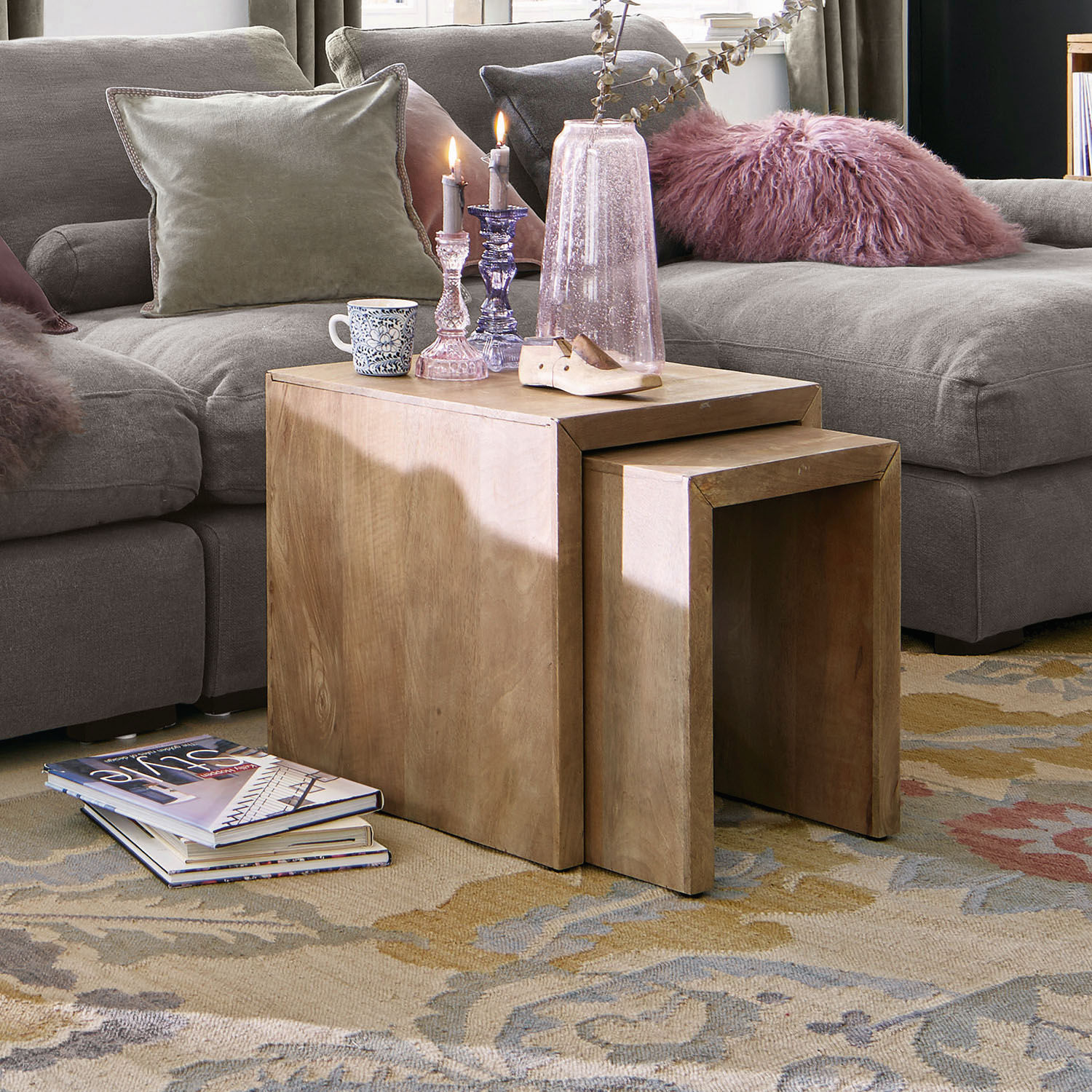 Zwei natürliche Holztische als Beistelltische auf Teppich vor grauem Sofa im Wohnzimmer