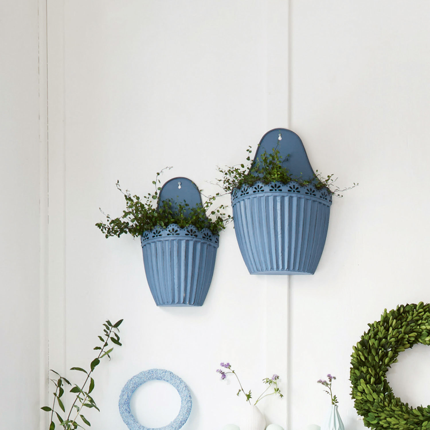 Zwei blaue Metall-Wandblumentöpfe mit grünen Pflanzen an weißer Wand, Wohnraumdeko