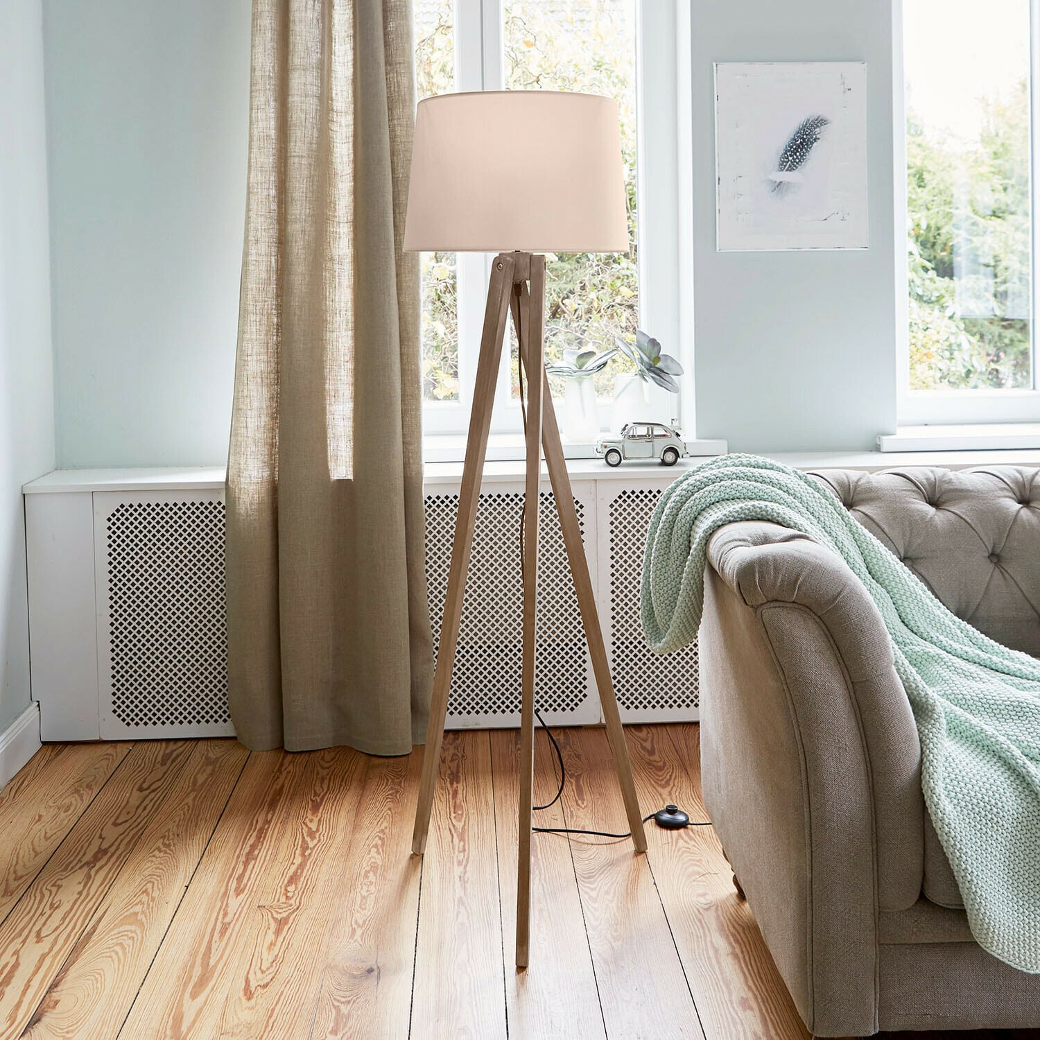 Stehlampe mit Holzgestell und cremefarbenem Lampenschirm in hellem Wohnzimmer mit Sofa und Decke