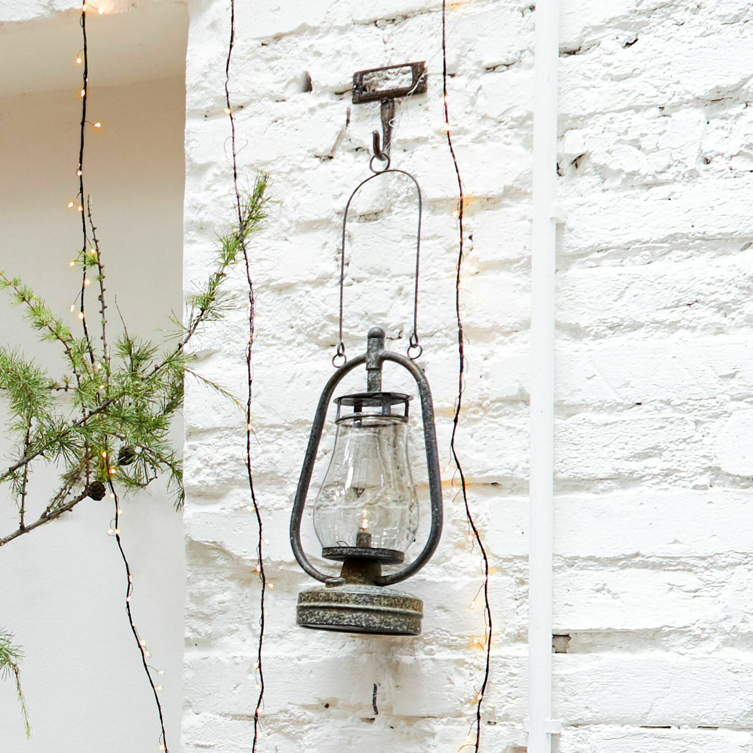 Hängende Metalllaterne mit klarem Glas an weißer Ziegelwand, Garten- und Wanddekoration