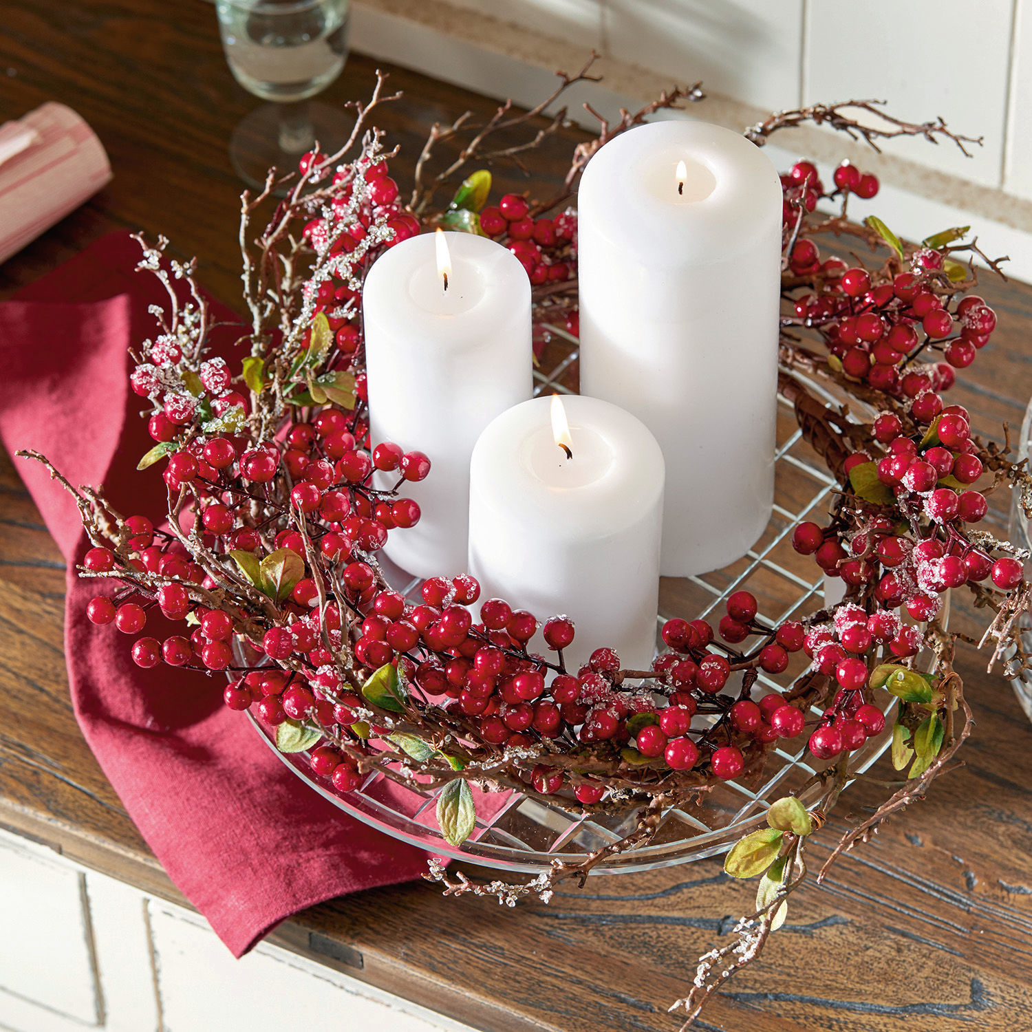 Dekorativer Kranz mit roten Beeren und drei weißen Kerzen auf Holztisch