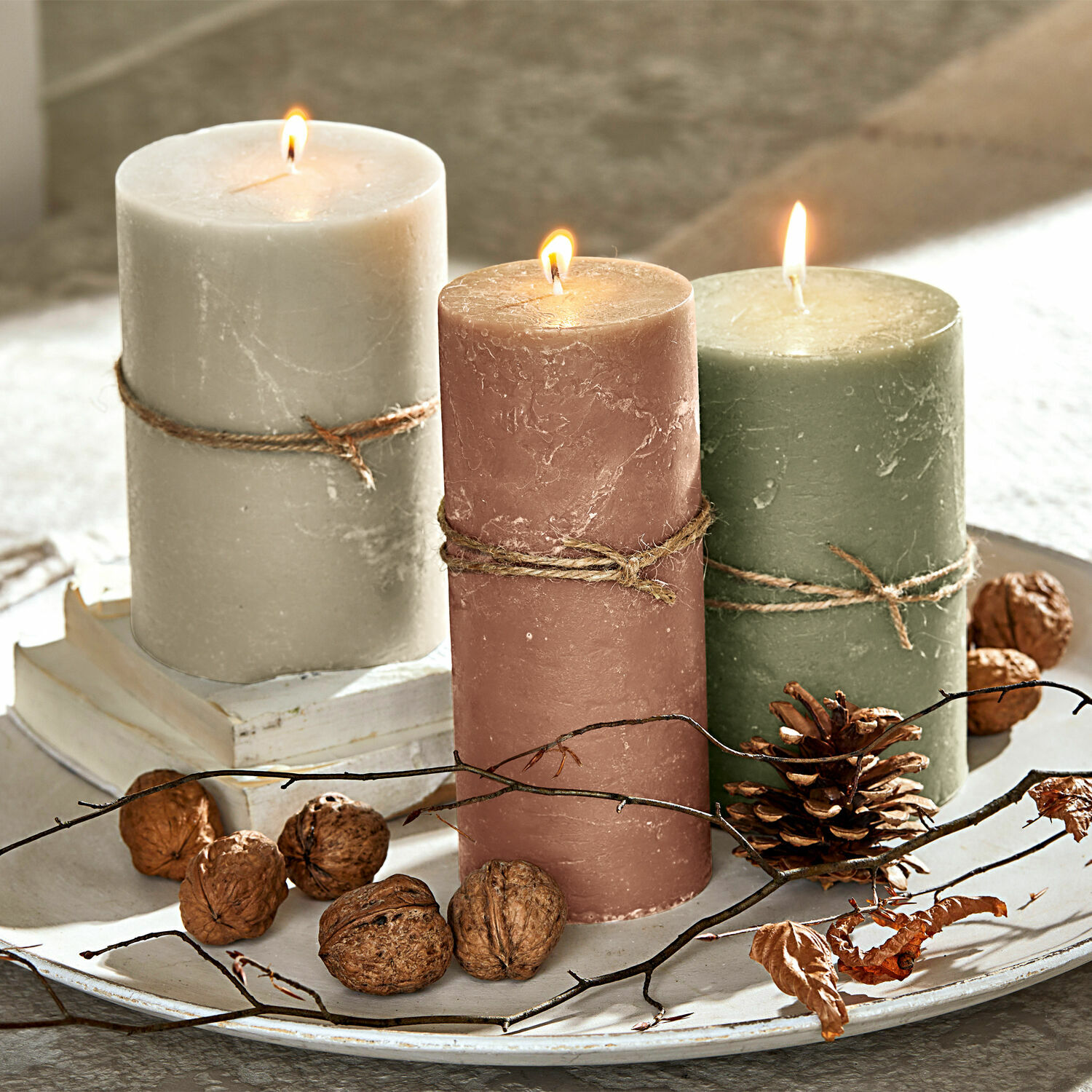 Kerze 3er Set Salis Drei brennende Wachskerzen in Beige, Rosa und Grün auf dekorativem Tablett mit Nüssen und Zweigen