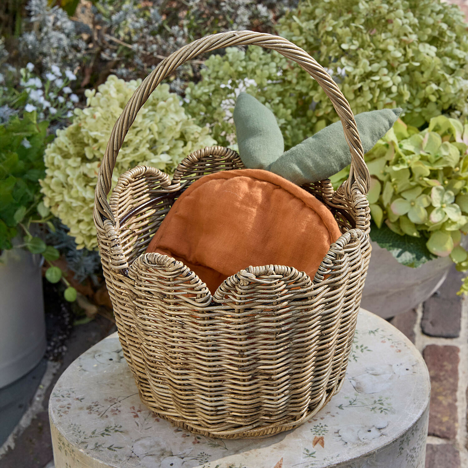 Korb Whimsywood Wikingerkorb mit orangefarbenem Kissen und grünen Blättern, Gartendekoration auf rundem Tisch