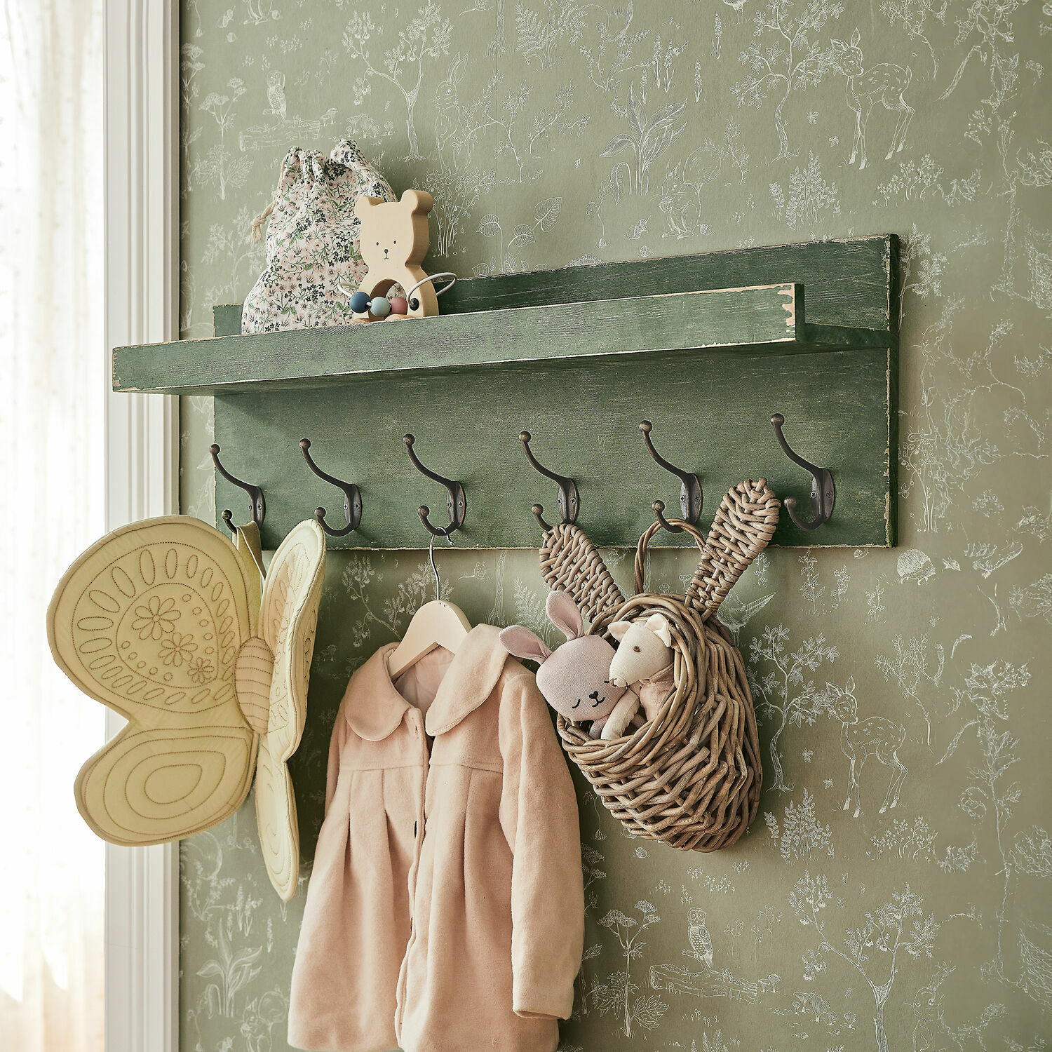 Wandregal Hoboken Grüne Holz-Wandgarderobe mit Haken, Kinderjacke und Korb mit Plüschtieren vor Tiermuster-Tapete