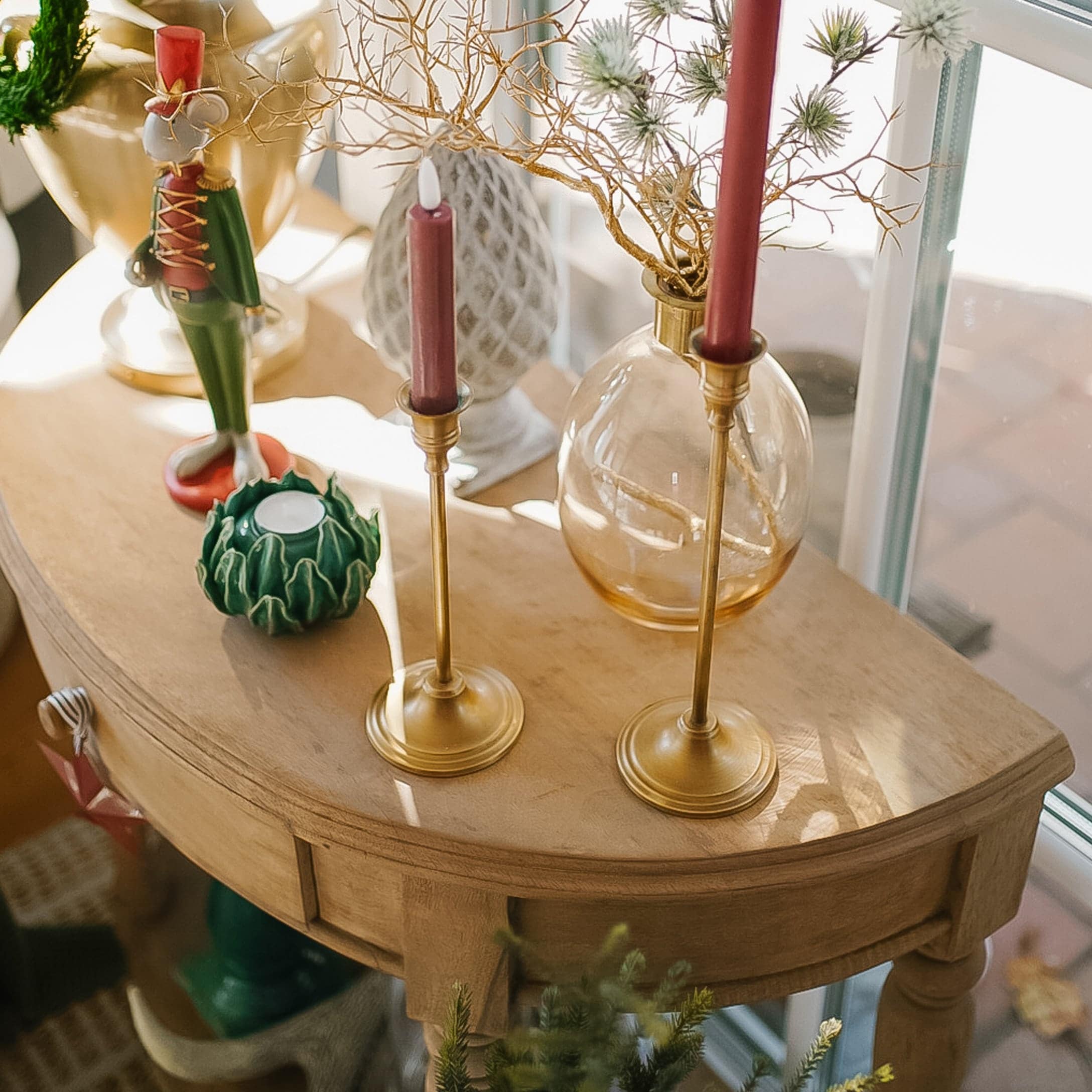Holztisch mit Messing-Kerzenhaltern und weihnachtlicher Dekoration im warmen Licht.