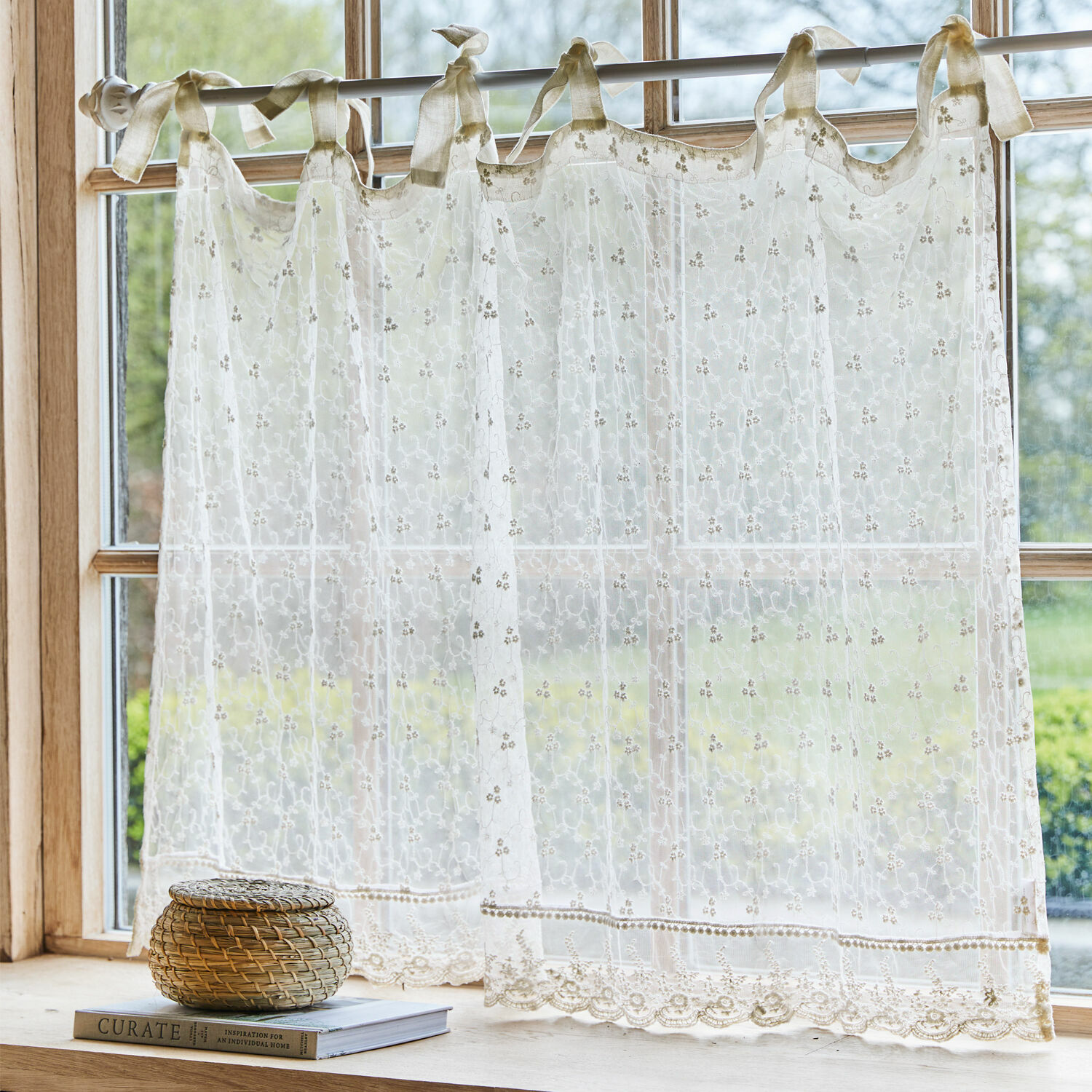 Scheibengardine Auradé Transparenter, bestickter cremefarbener Vorhang mit Schleifen an einem Fenster mit Gartenblick