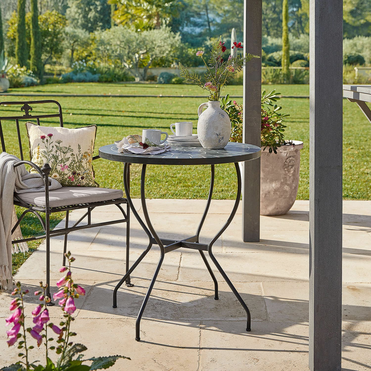 Tisch Ballaigues Runder Gartentisch mit Metallgestell und grauer Mosaikplatte auf sonniger Terrasse