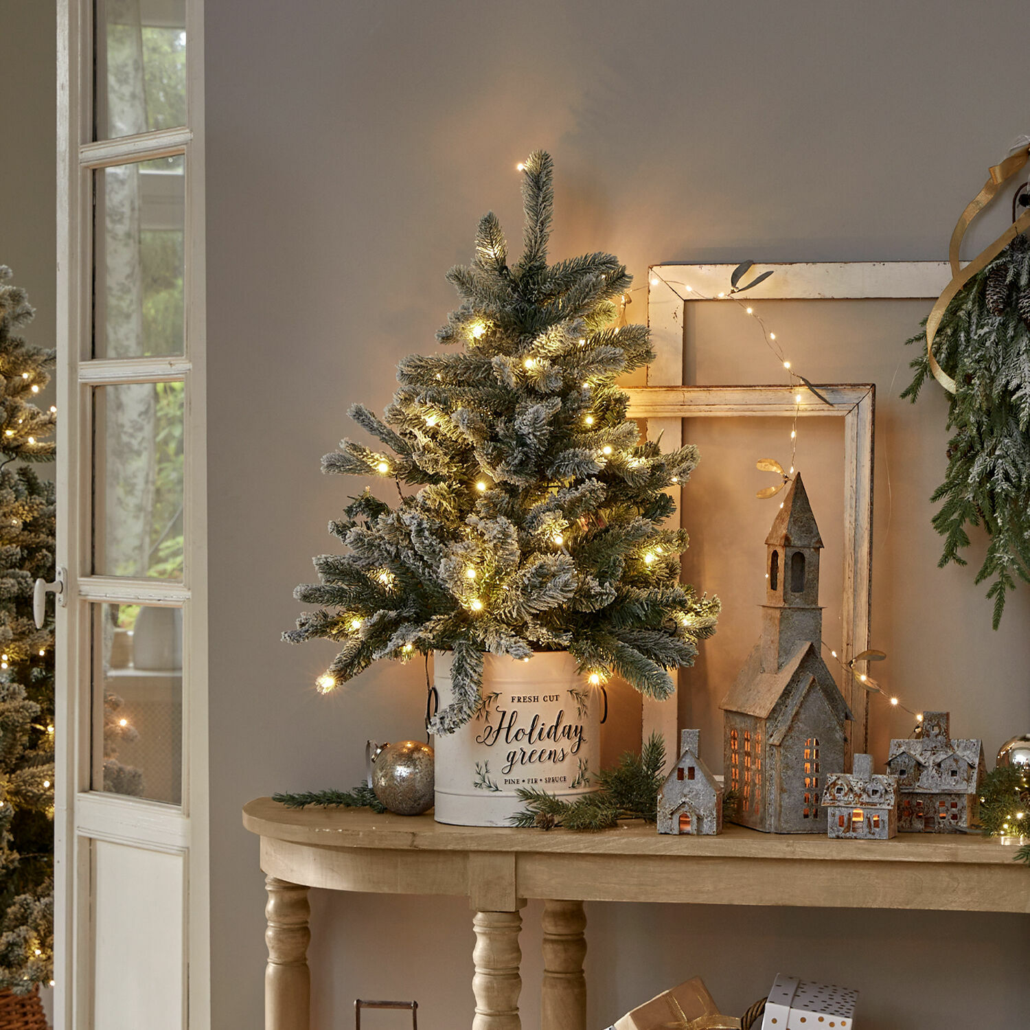 Weihnachtsbaum Mannier Weihnachtsdekoration mit beleuchtetem künstlichem Tannenbaum in weißem Metallkübel auf Holztisch