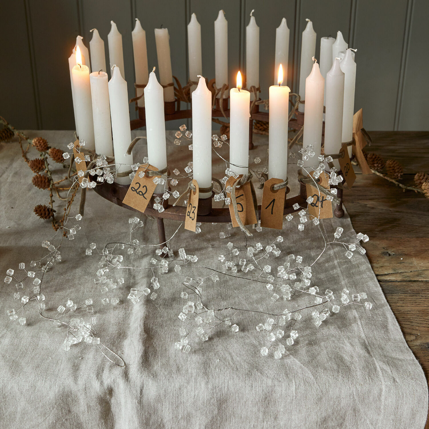 Metall-Adventskranz mit weißen Kerzen und Papieranhängern auf Leinentuch, festliche Weihnachtsdekoration